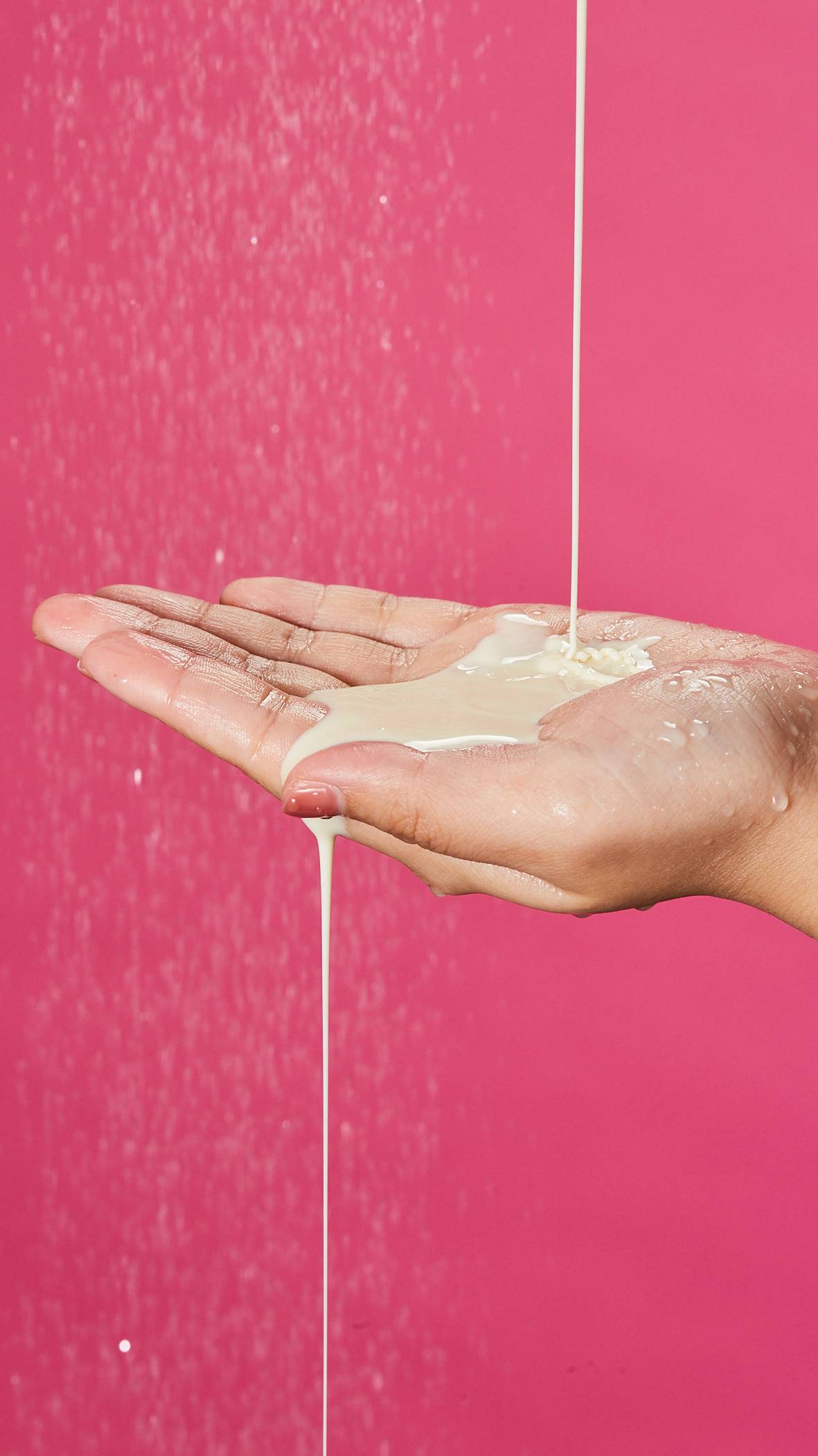 A close-up of the model's hand which is being filled with a generous amount of the Sakura shower gel from above and is overflowing on a deep pink background. 