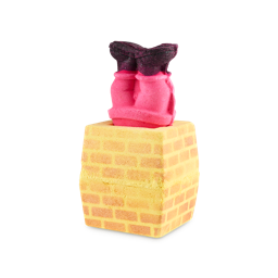 Stuck In The Chimney 3-in-1 bath bomb. The image shows a cuboid bath bomb shaped like a yellow brick chimney. A removable figure's red-suited legs and black boots stick out of the top.