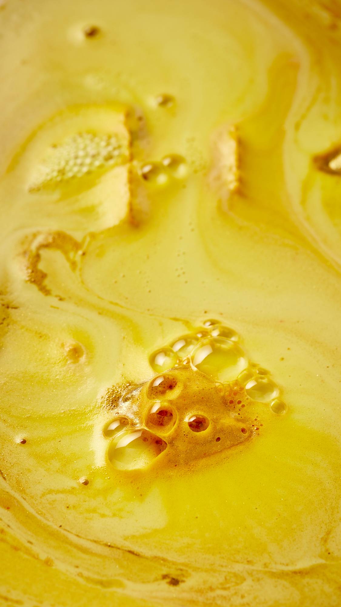 A close-up shot of the festive, Santa's Postbox bath bomb as it has nearly fully dissolved. There is thick, velvety, bright yellow foam laced with gold, shimmering lustre. 