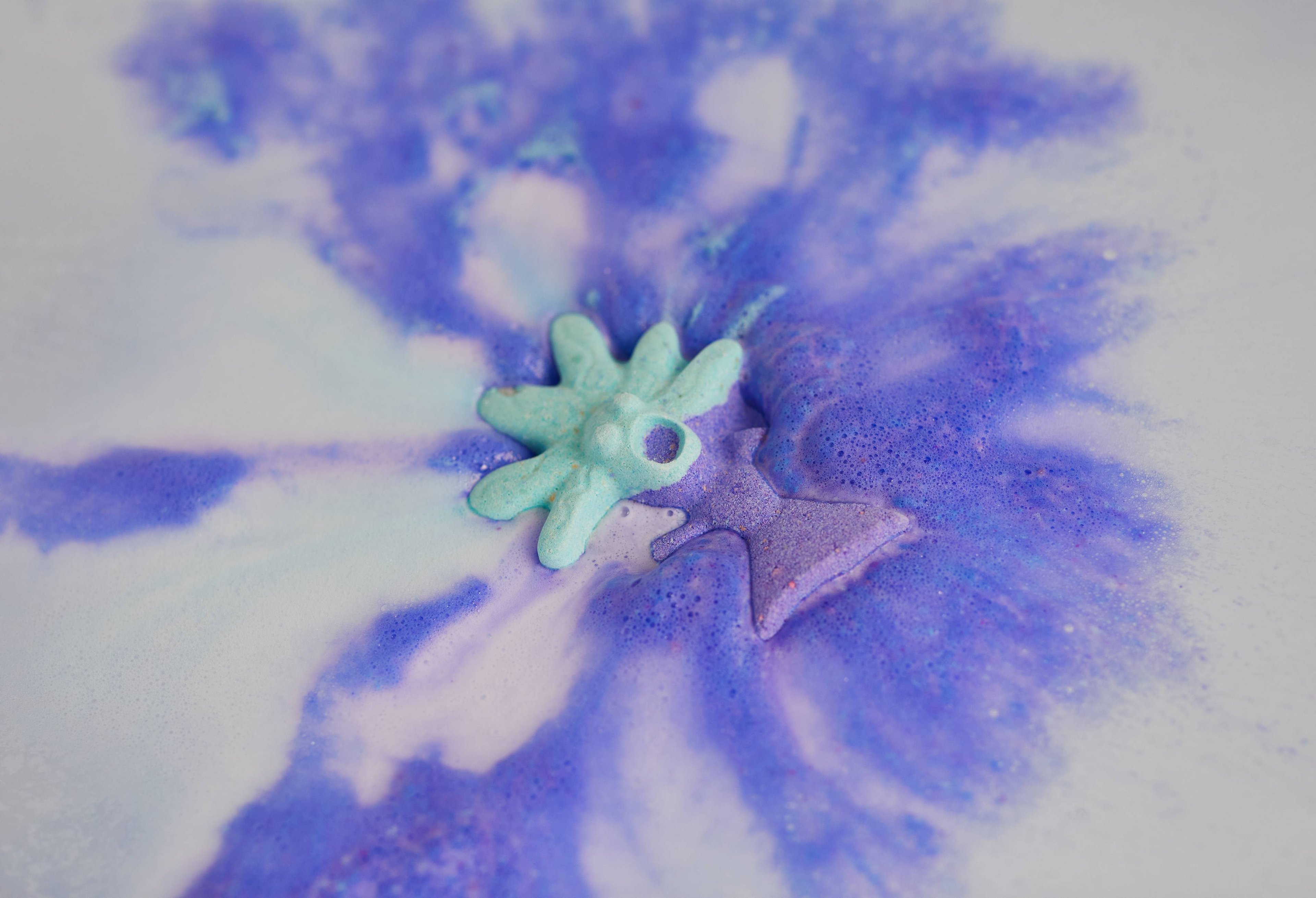 Bath bomb floats on the water, releasing foaming swirls of mystical blue and purple. 