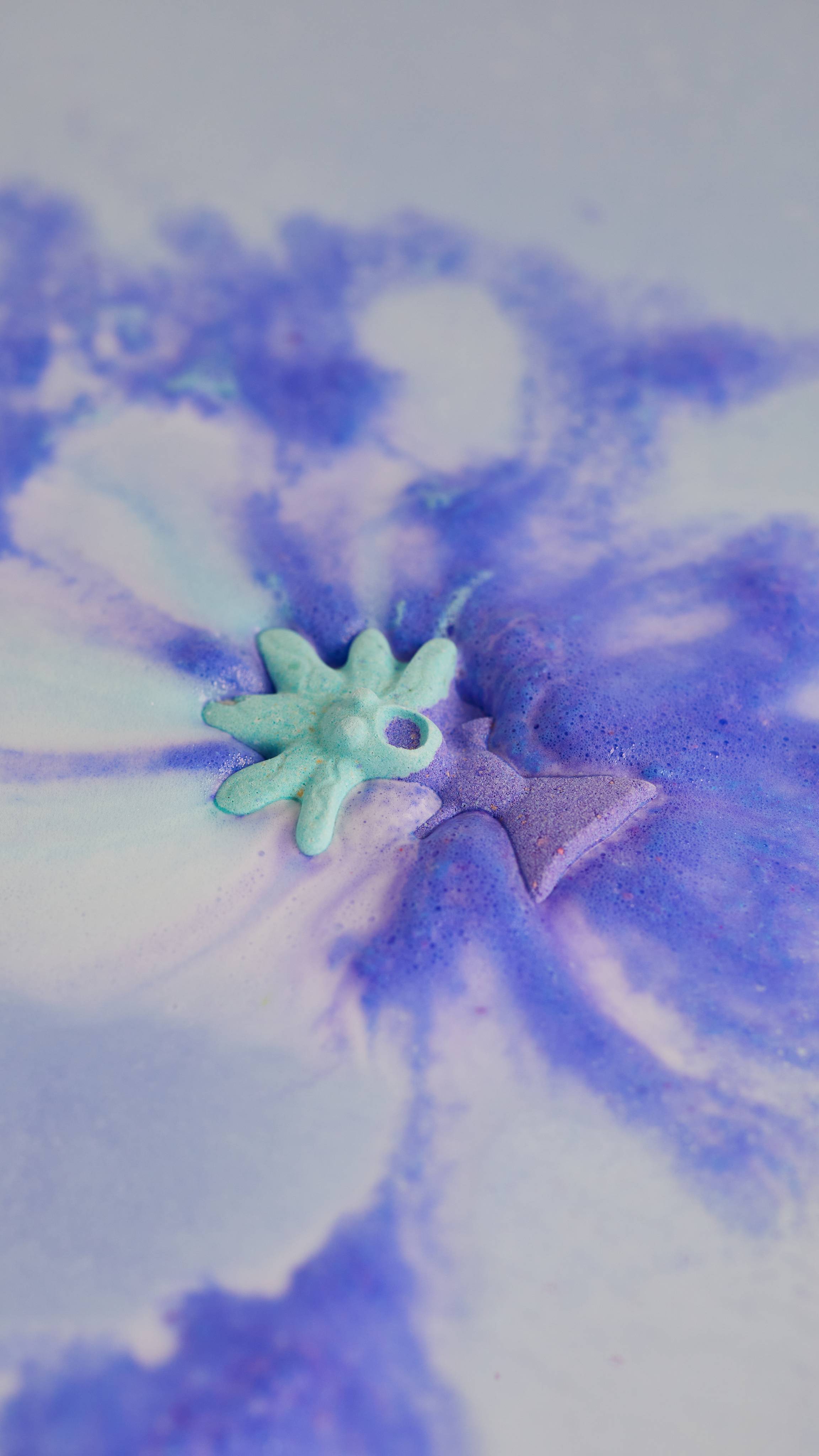 Bath bomb floats on the water, releasing foaming swirls of mystical blue and purple. 
