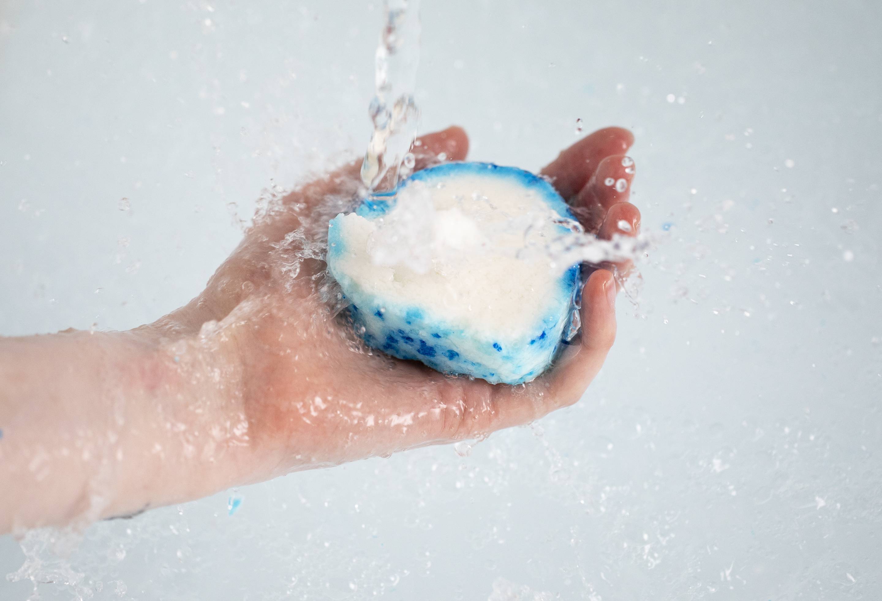 A close-up image of the model's hand holding the Seaside bubble bar under running tap water.