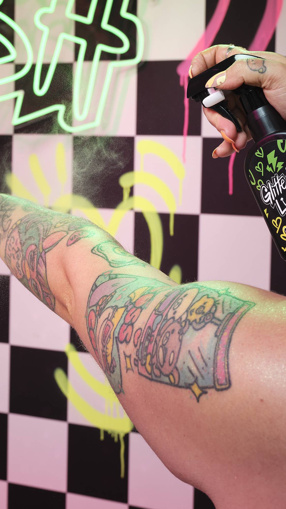 A close-up of the model spritzing the body spray on their arm in front of a checkered wall with neon graffiti.