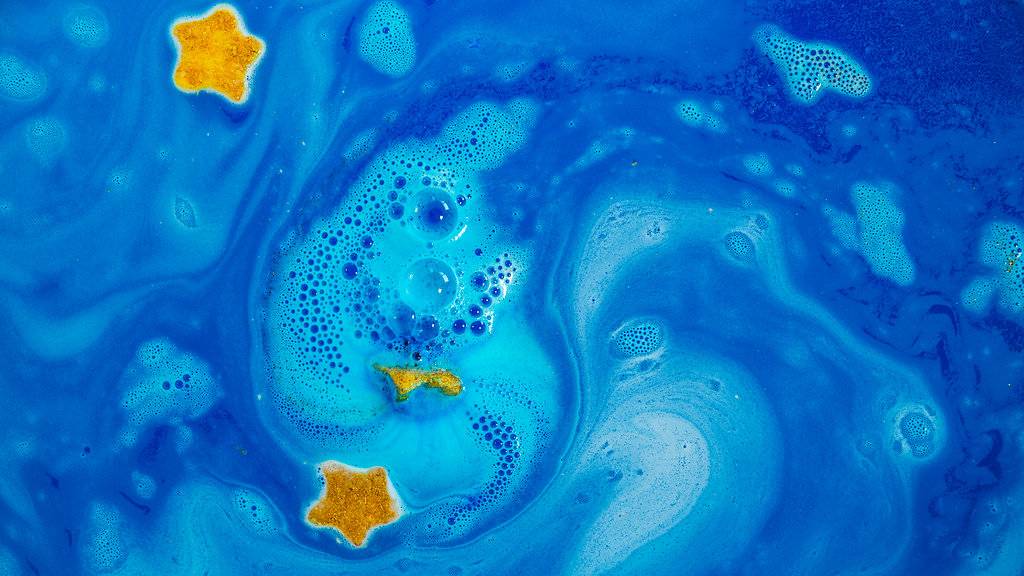 A view of the water from above shows a swirling, deep-blue, galaxy sea with shimmering, golden stars.
