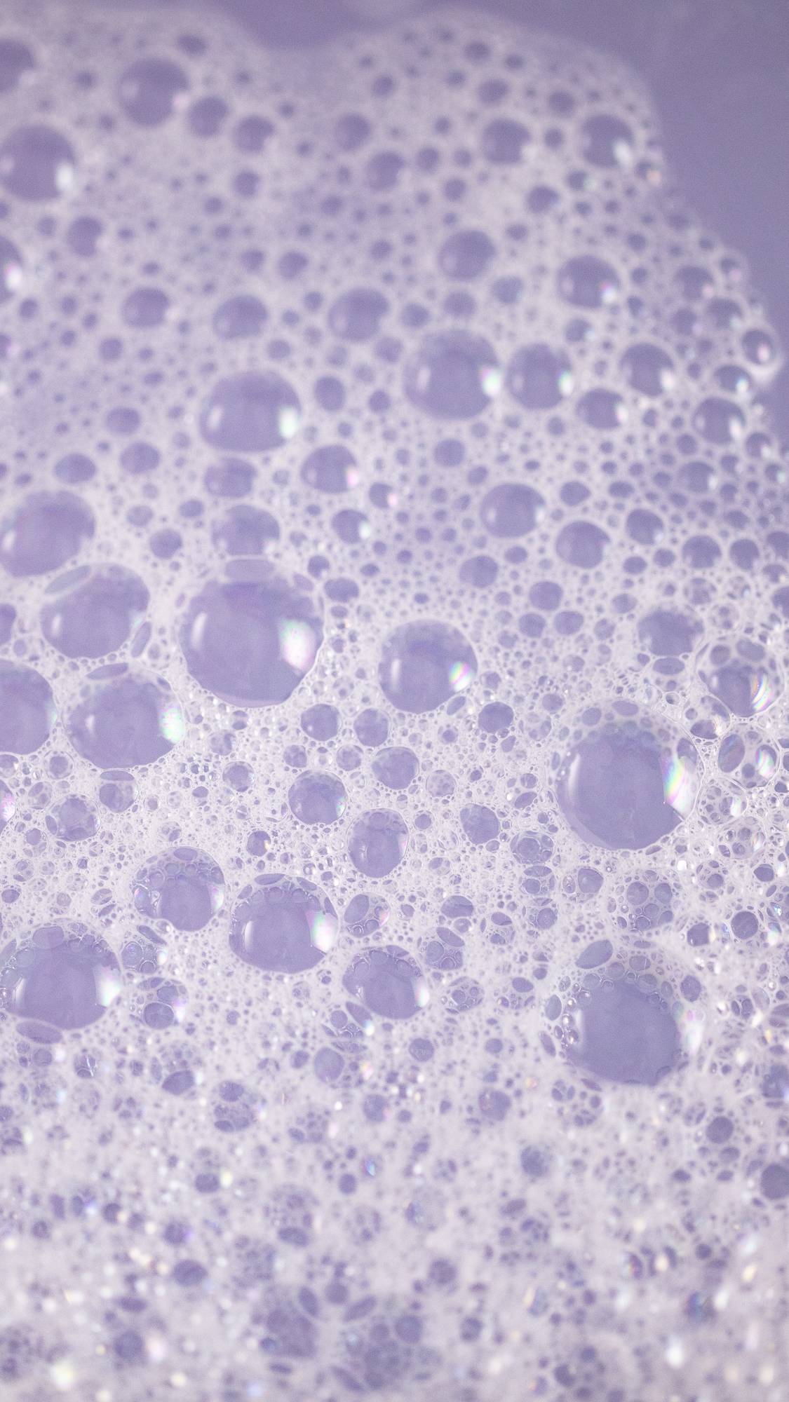 The image shows a close-up of the bath water as it has been coloured a delicate lilac with a carpet of velvety bubbles on top.