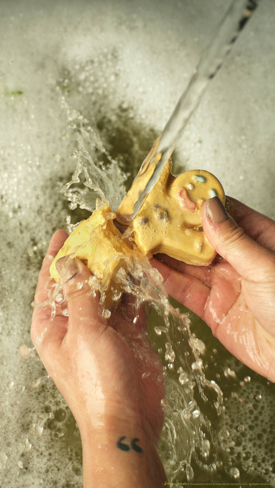A close-up of the model's hands as they break the Gingy bubble bar in half and hold it under running tap water to create mountains of bubbles below. 