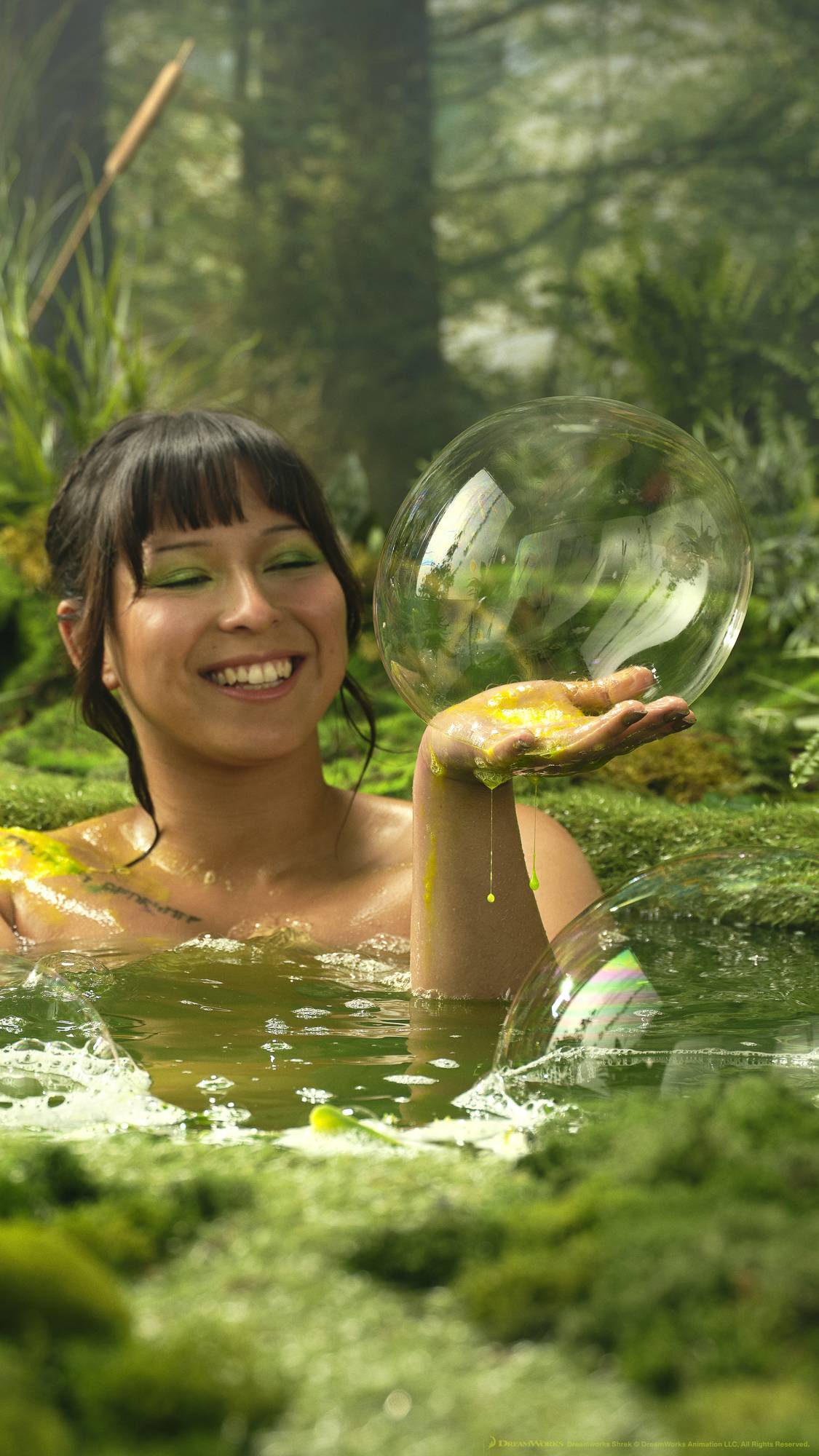The model is sat in the pond with the water to their shoulder as they use the Fiona shower gel. They have managed to form a large, single bubble from the product on one hand. 