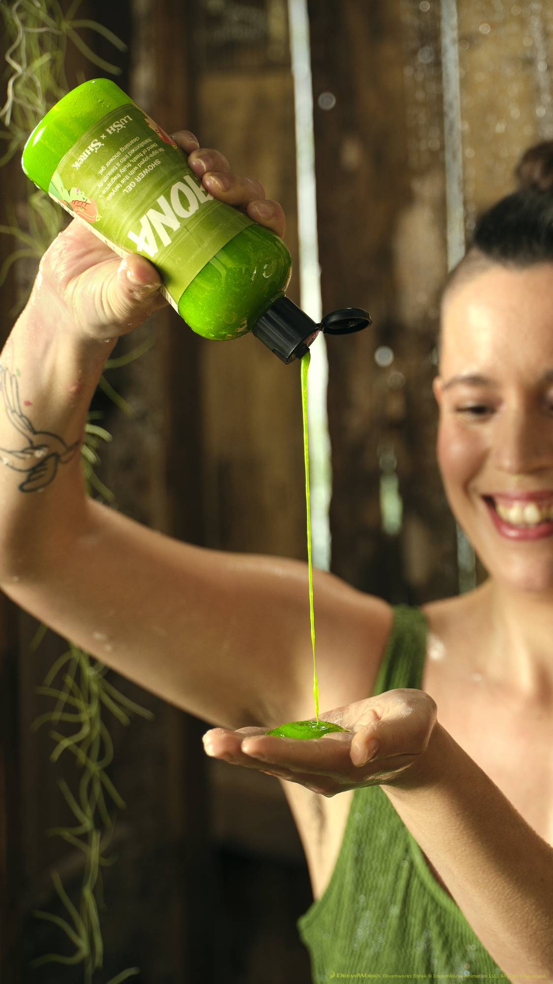 A close-up shot of the model in the wooden outhouse squeezing the bright green Fiona shower gel product from the bottle into their hand. 