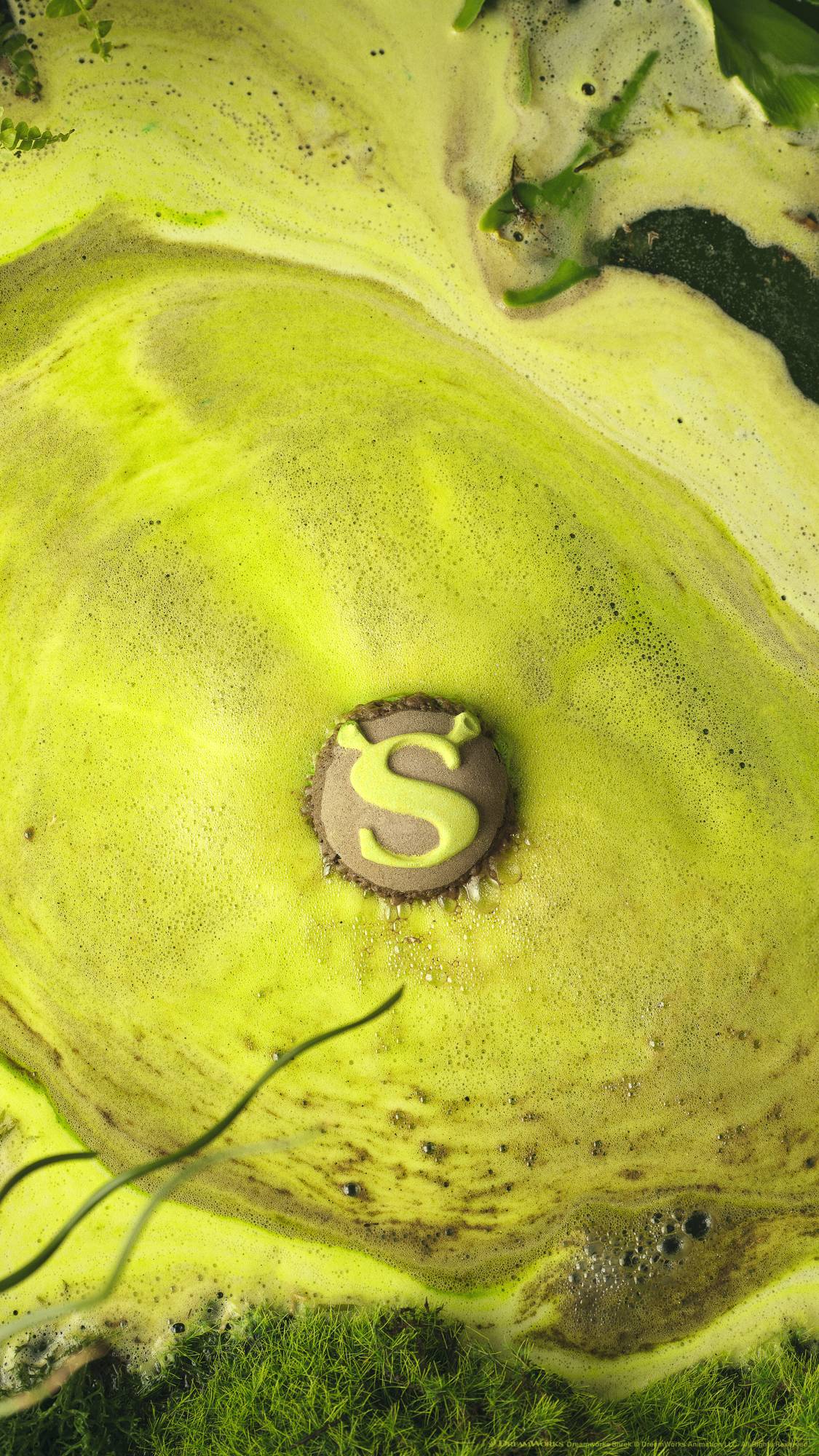 The Shrek Swamp bath bomb slowly dissolves on the water's surface releasing thick, velvety swirls of bright, lime-green foam with flecks of brown.