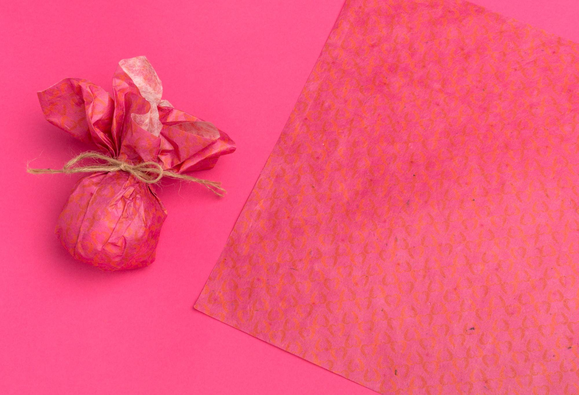 The lokta wrap is wrapped around a bath bomb, as well as laid out flat, on a bright pink background.