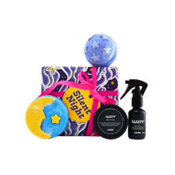 A Lush "Silent Night" gift set wrapped in starry paper with a pink ribbon and yellow tag, surrounded by Sleepy body spray, Sleepy body lotion, a blue starry bath bomb, and a crescent moon bubble bar