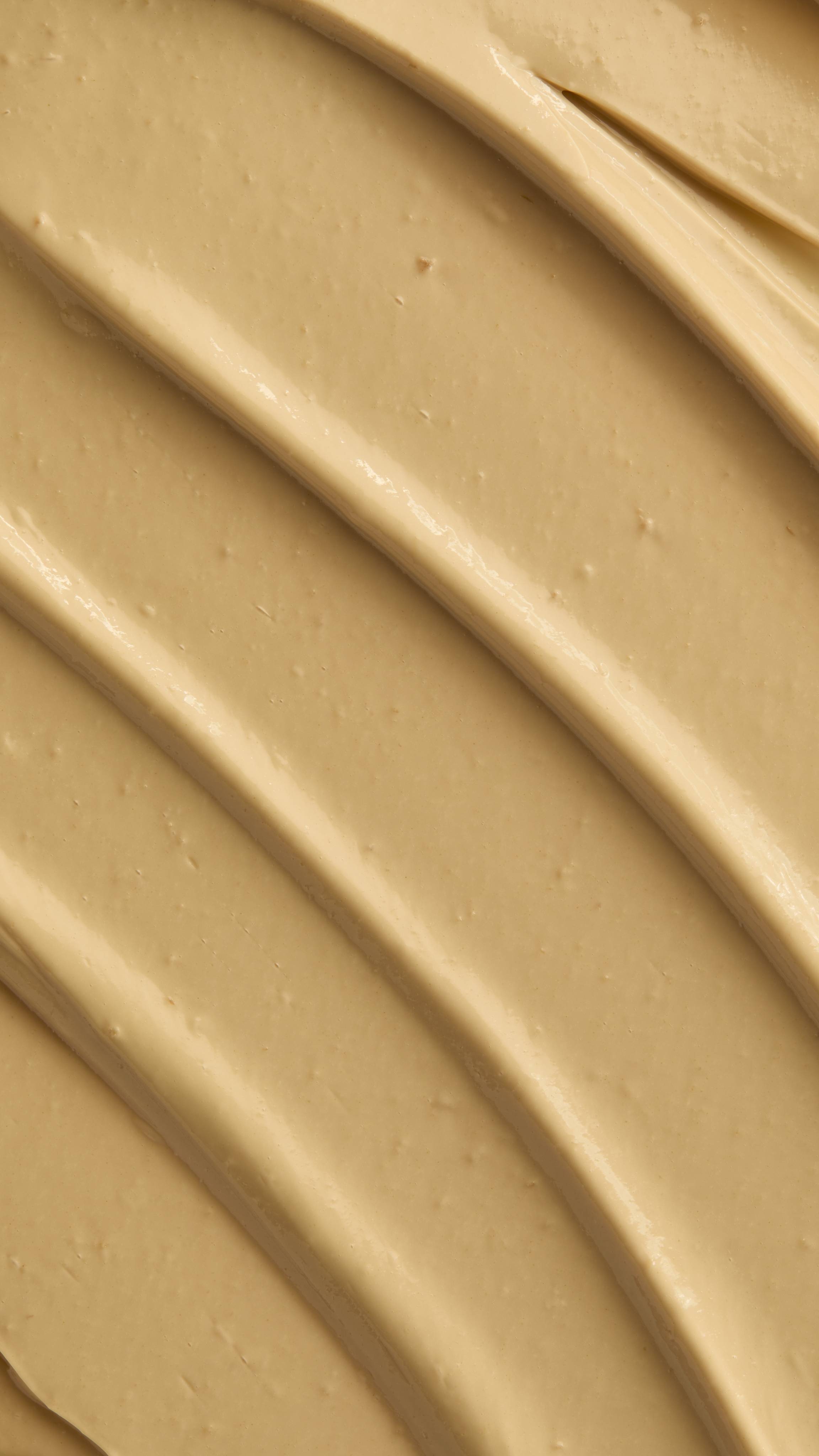 A macro texture shot showing the ridges of skin drink, beige cream spread in diagonal lines.