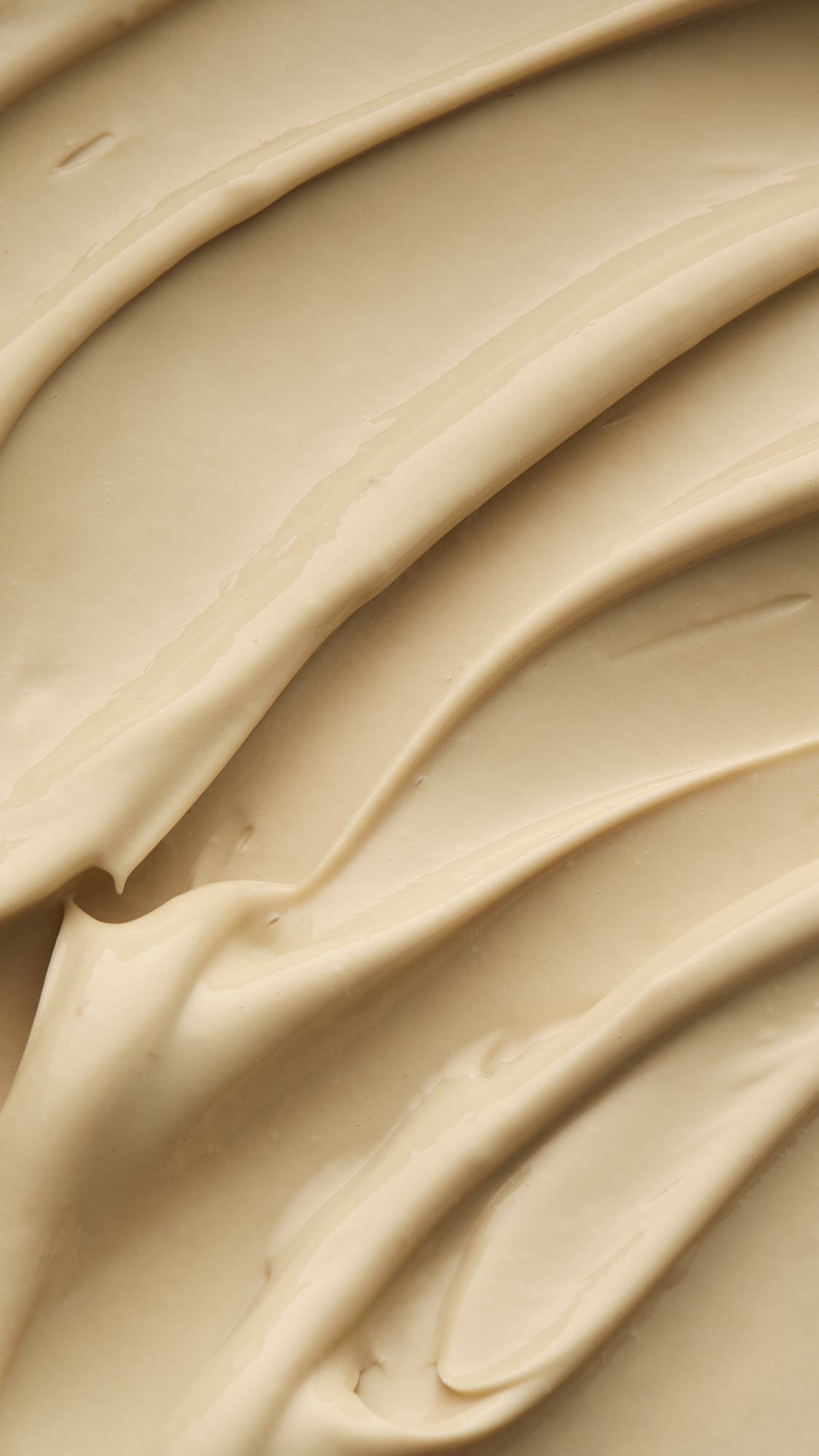 A super close-up of the Skin Drink self-preserving moisturiser focusing on the thick, creamy, texture of the honey-coloured product. 