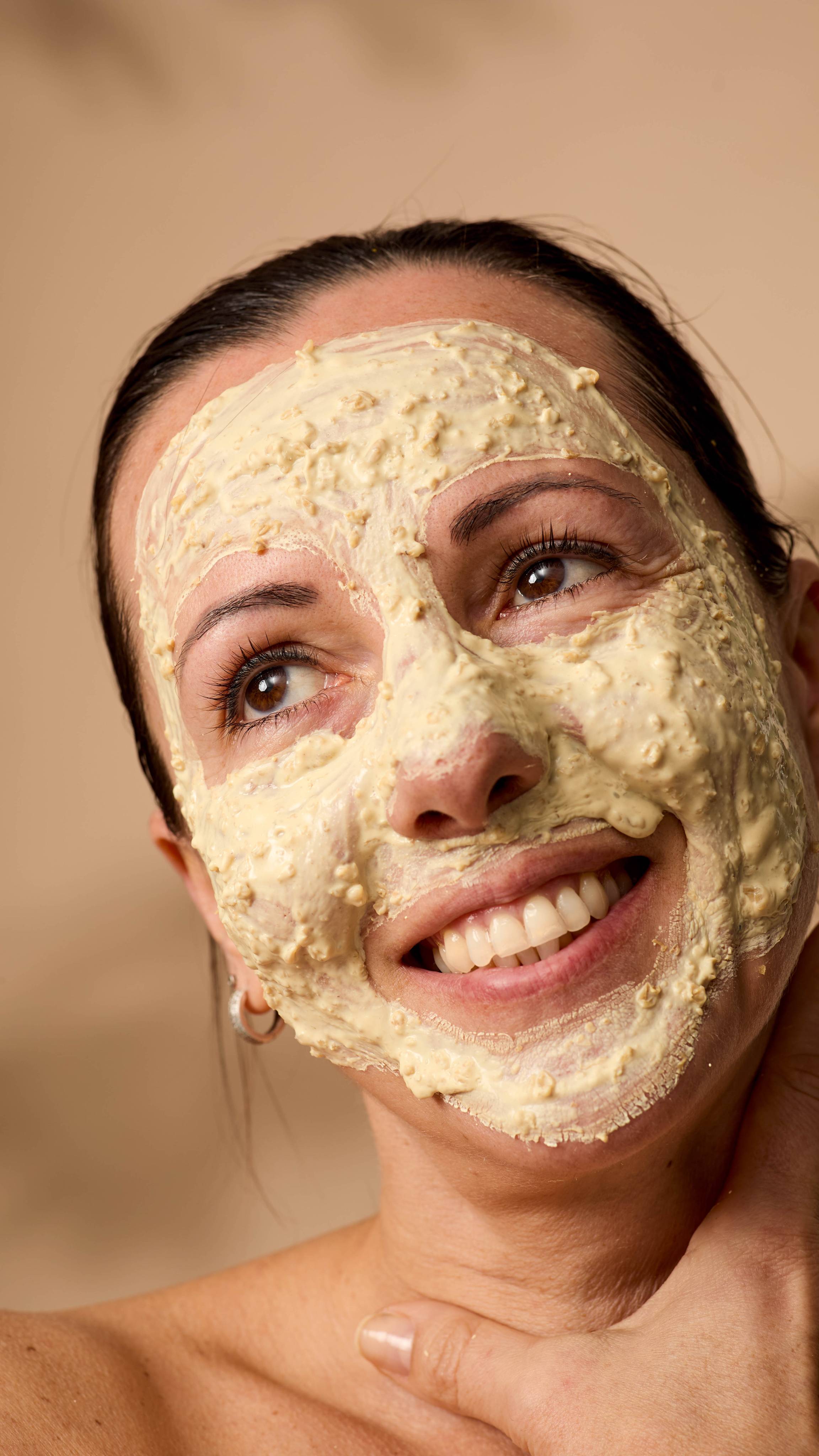 A close-up of the model's face coated in the Skin Soothing Porridge face mask with visible oats sprinkled throughout.
