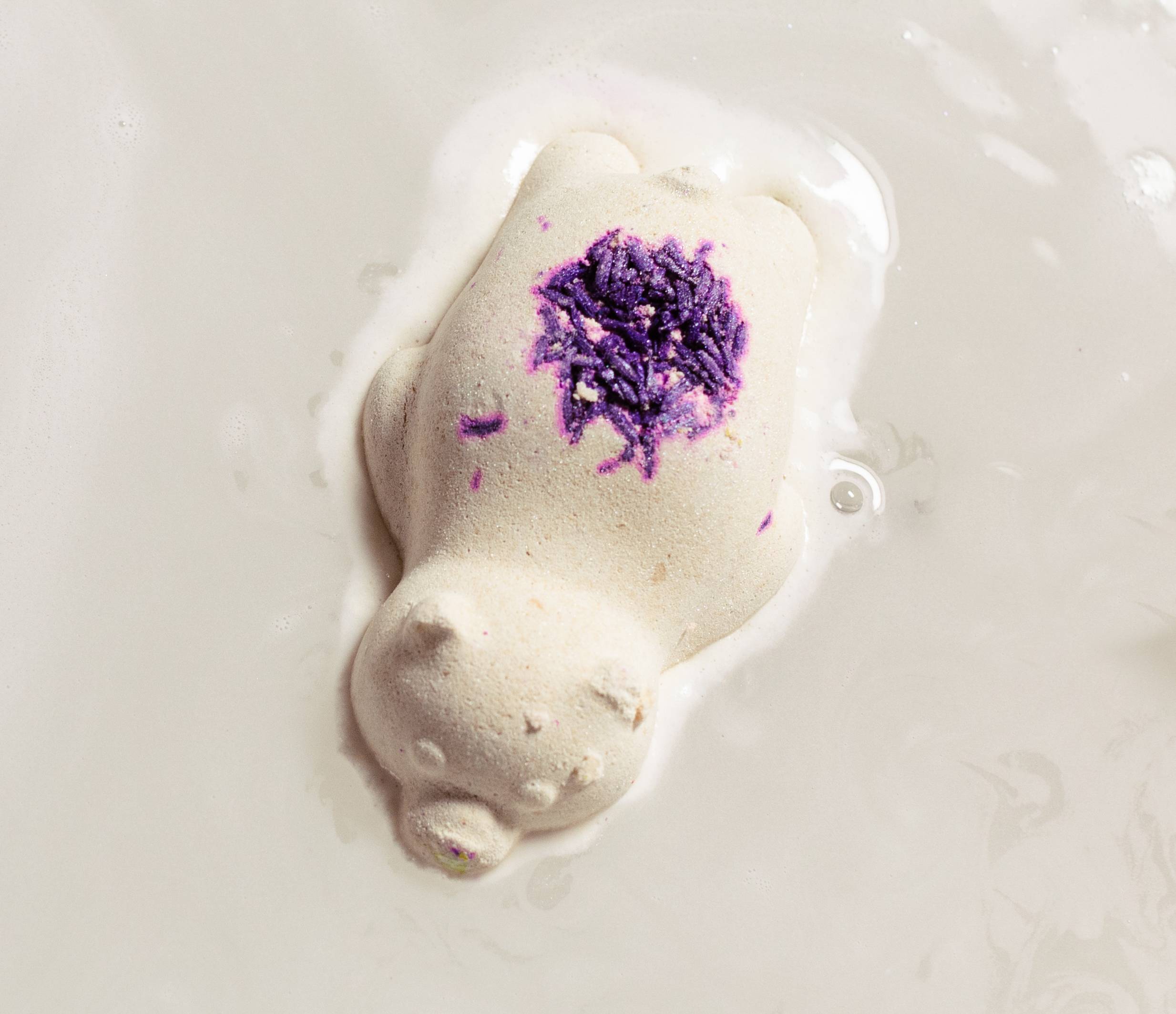 Image shows the Sleepy Bear bath bomb laying on top of water with luscious, creamy foam dispersing all around.