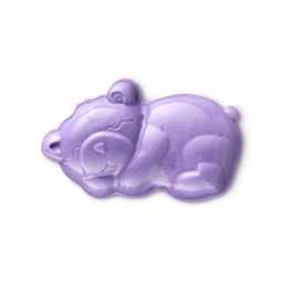 A glossy, purple, teddy bear-shaped LUSH Sleepy bear shower jelly is shown against a light gray background. The product is lying down with an engraved smiling face.