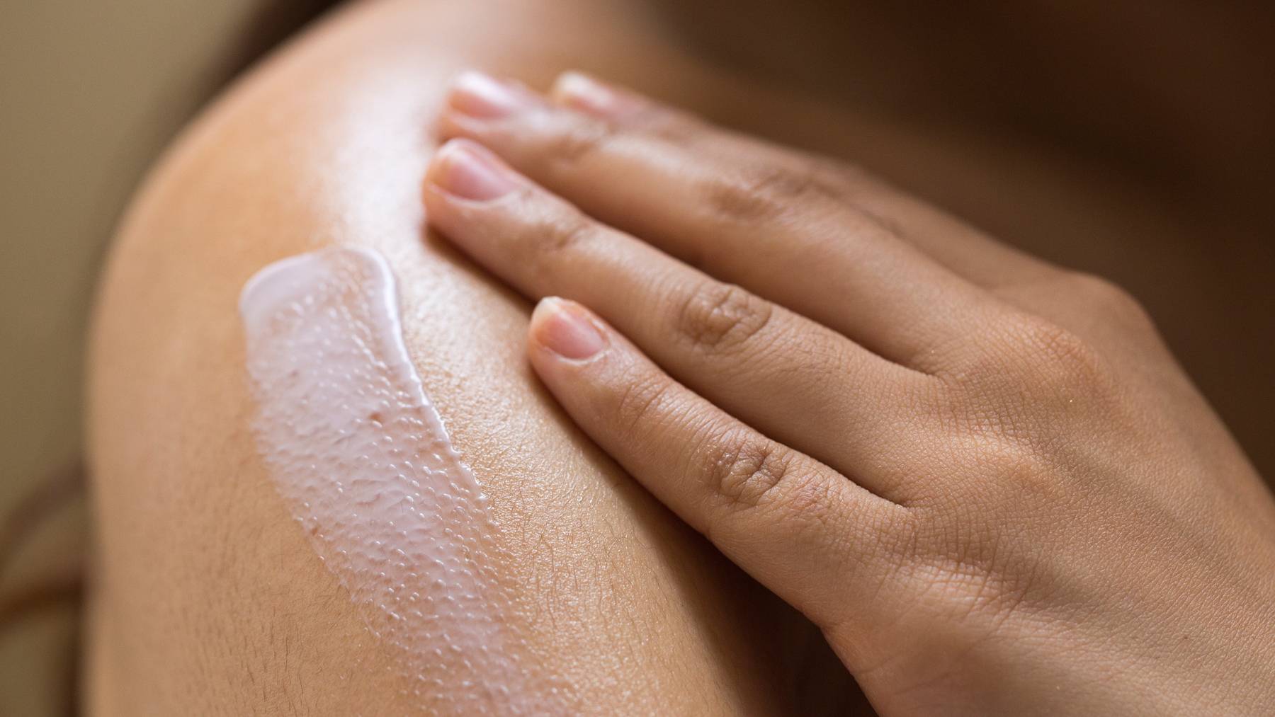 A stroke of Sleepy, a lilac coloured body lotion, rests on a person's shoulder, waiting to be rubbed in by their nearby hand.