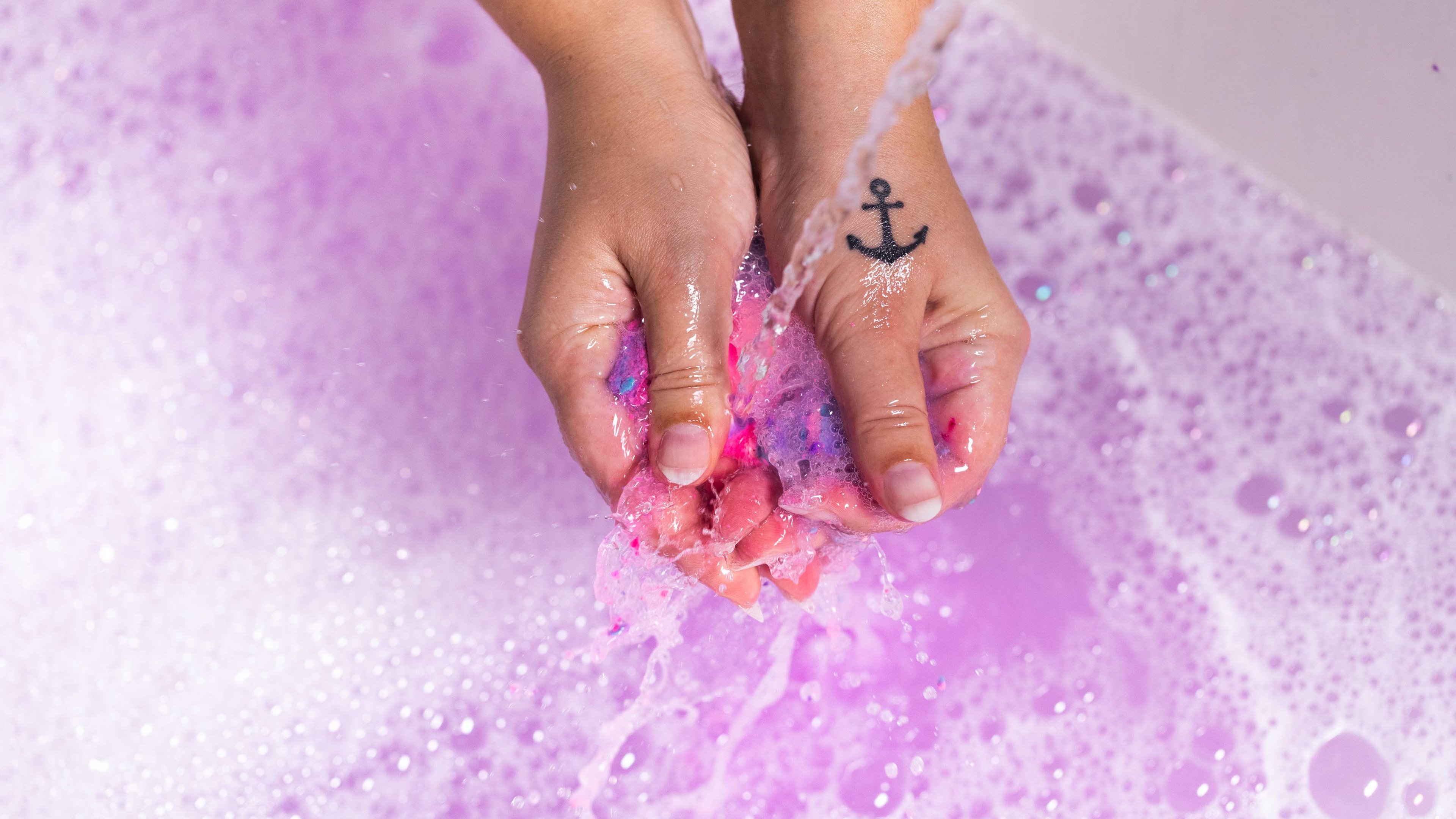 The image shows a close-up of the model's hand gently crumbling the mini Sleepy bubble bar under running water. 