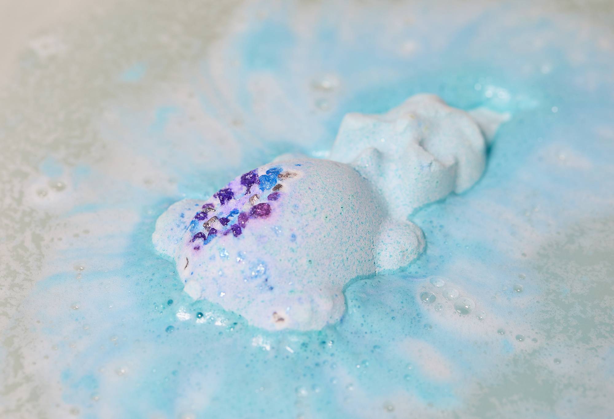 Snow Dragon bath bomb is half dissolved in the water as it gently releases pastel blue foamy swirls.