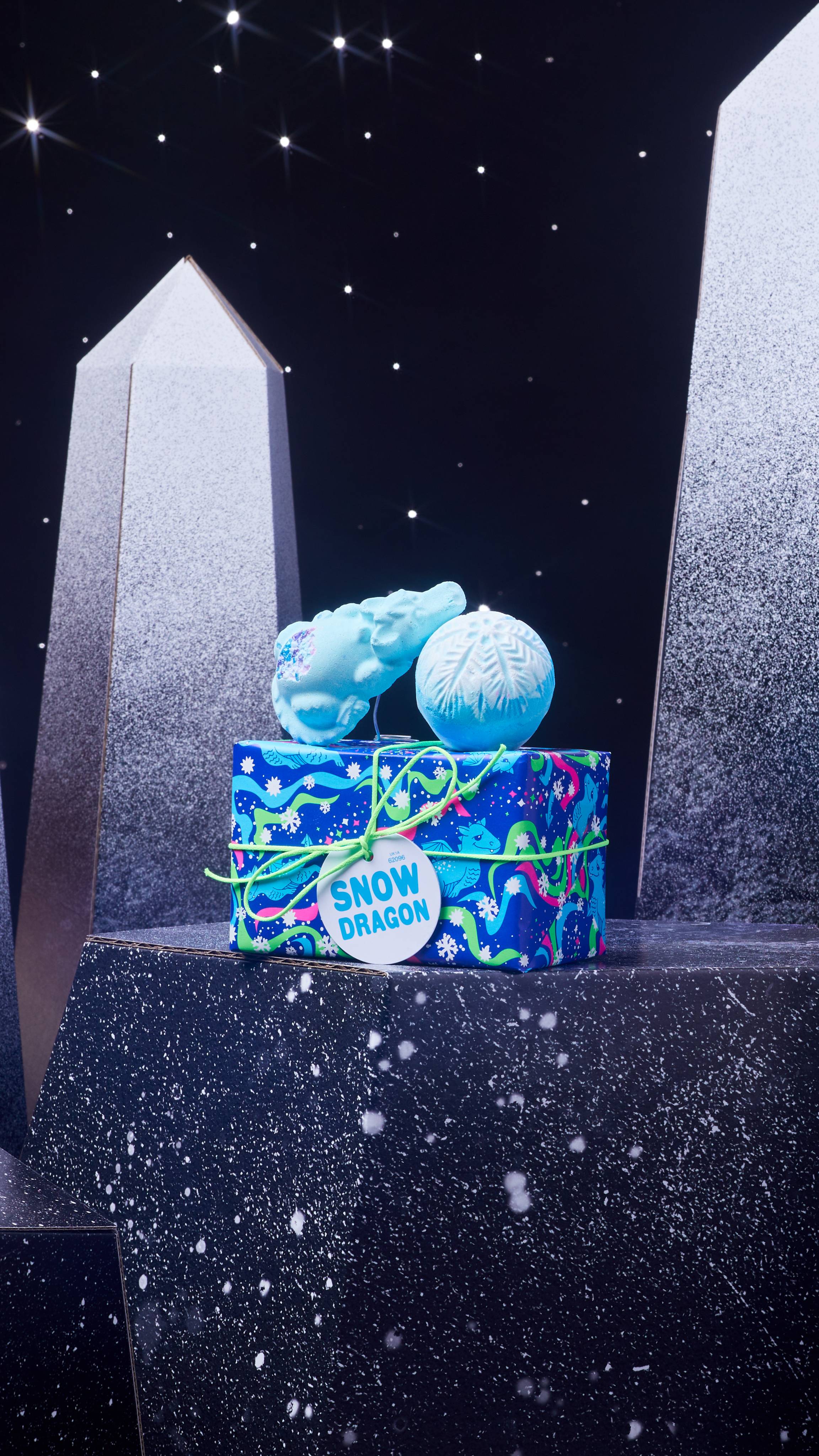 Snow Dragon gift box and it's two included bath bombs are on a dark chromatic platform among geometric shapes. 