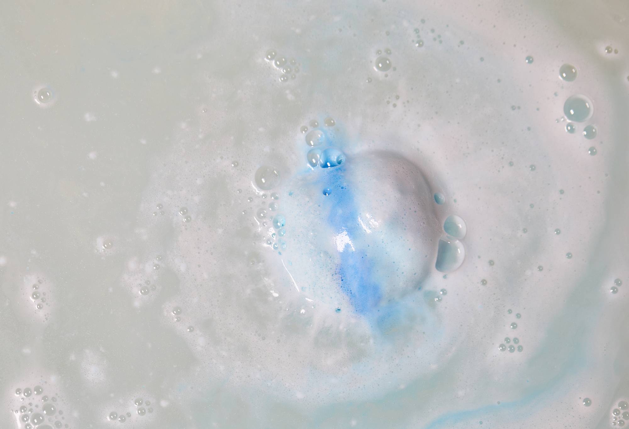 Image shows the Snowdrift bath bomb fizzing away in bathwater creating a delicate blanket of white and blue foam.