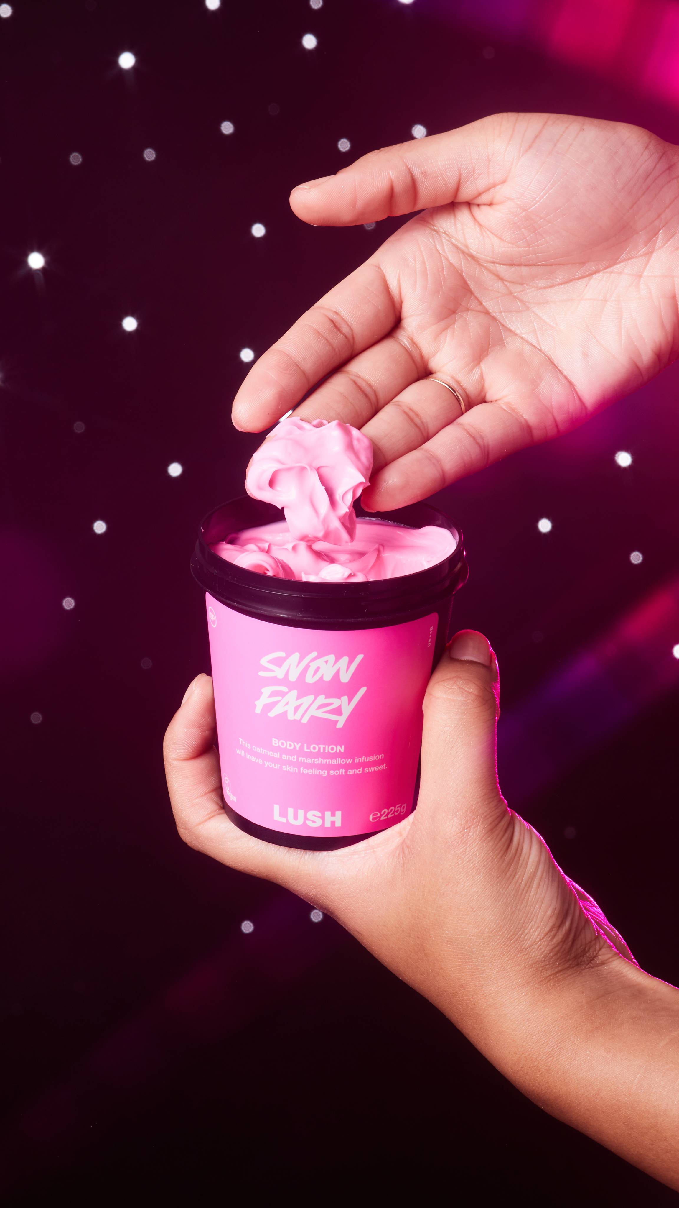 A close-up of the model holding the Snow Fairy body lotion pot as they gently scoop some out.