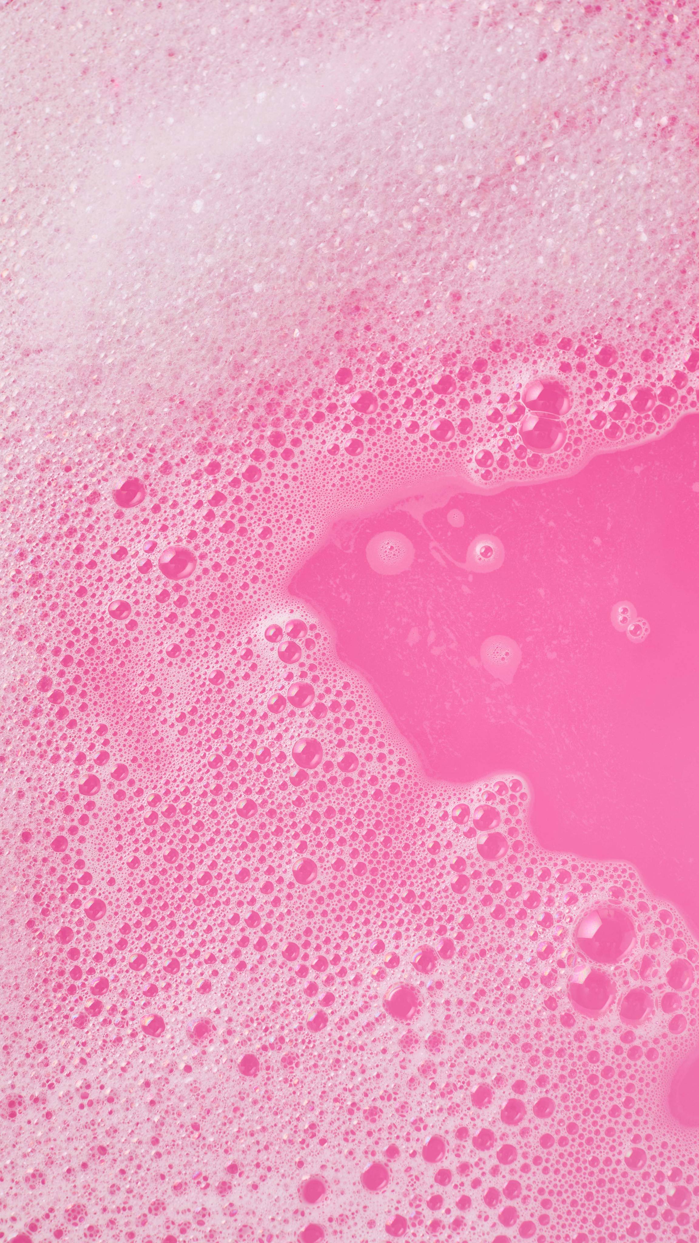 A close-up, aerial image of the bath water after using the Snow Fairy Bubble Mountain bubble bar. There is a blanket of thick, fat bubbles with bright, bubblegum-pink bath water visible through a large gap.