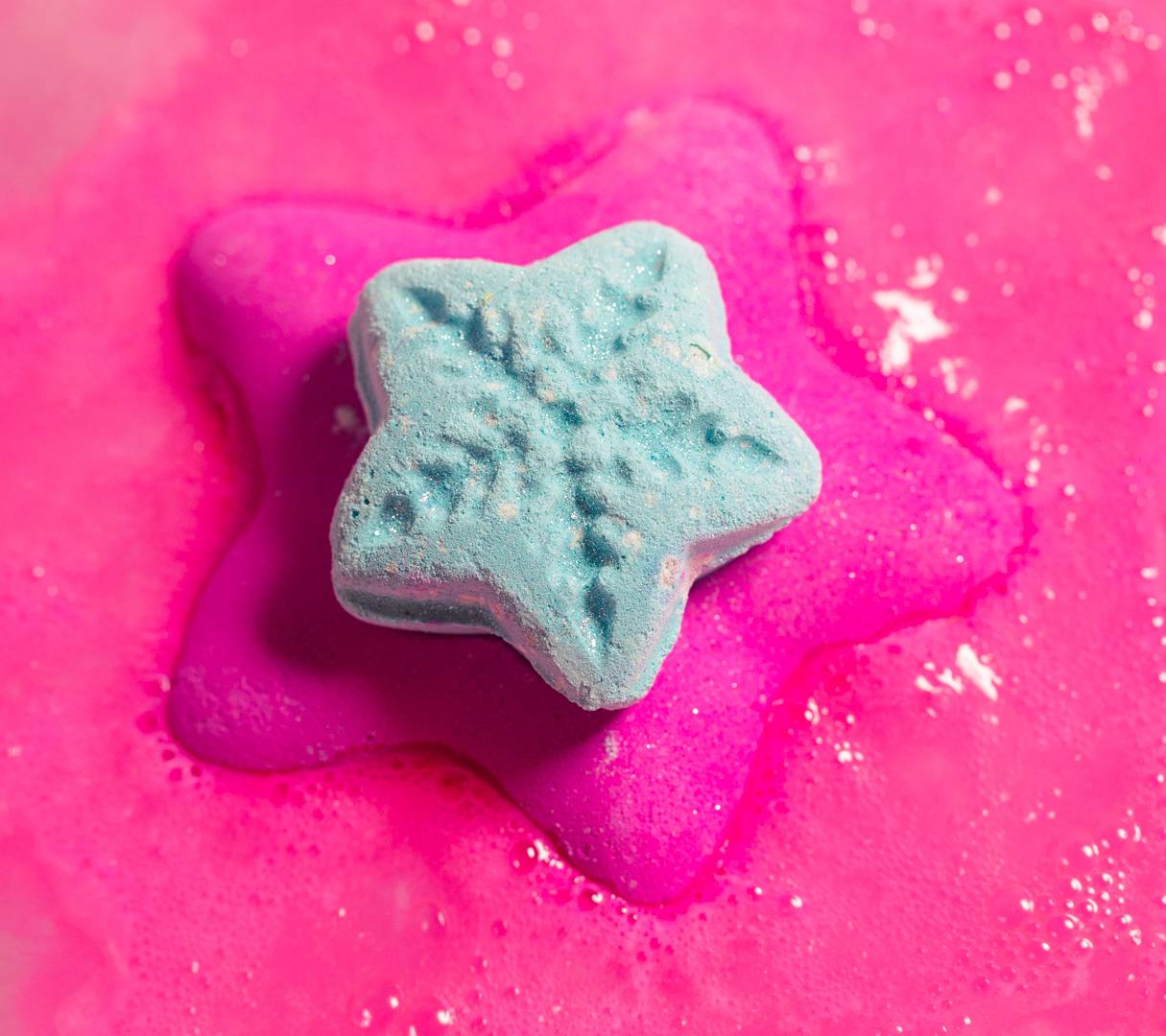 Snow Fairy Lights bath bomb floats on the water casting out a blanket of vibrant, hot-pink foamy swirls.