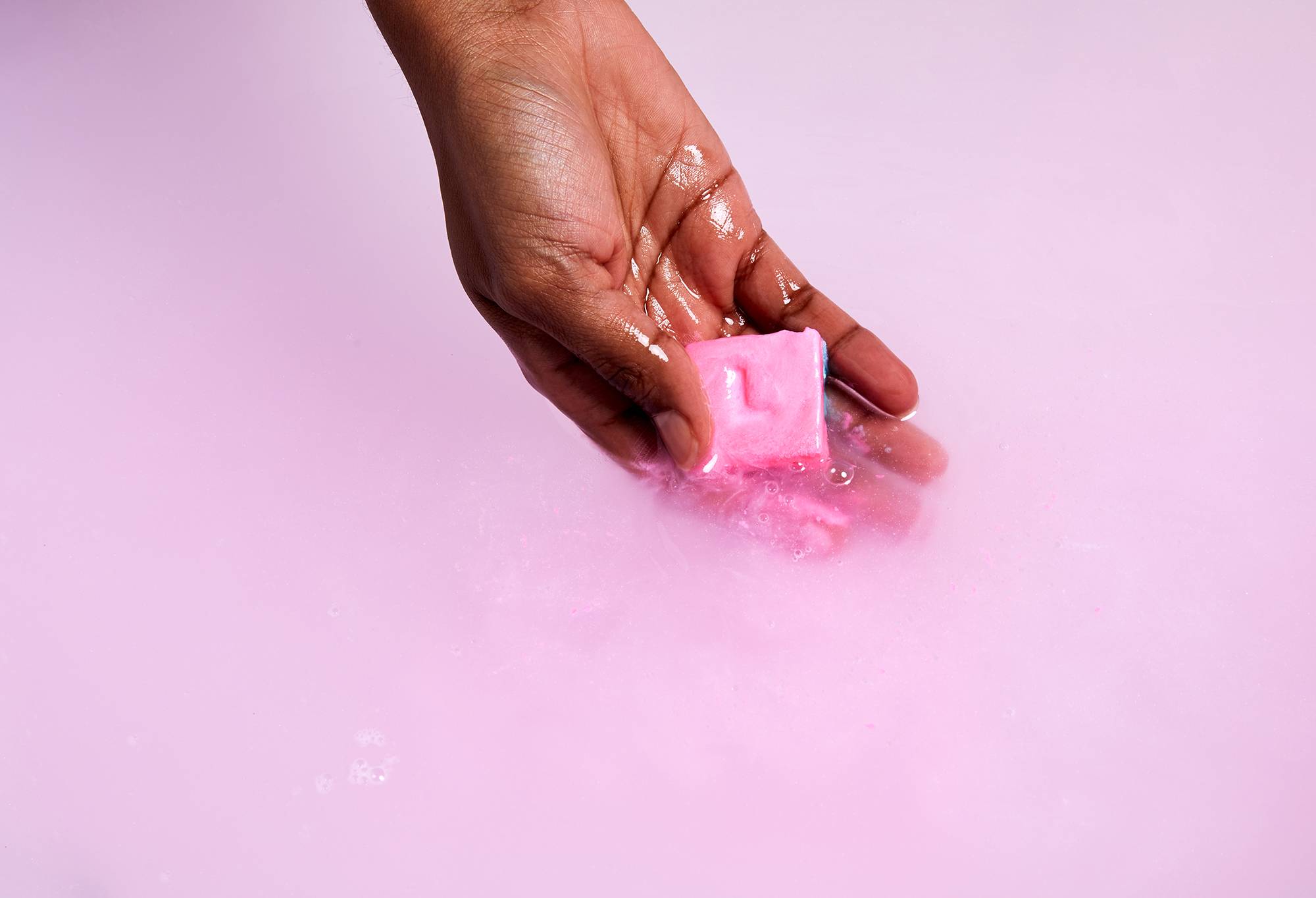 Image shows the model holding the Snow Fairy Lush melt in bathwater as it releases pink, hydrating oils. 