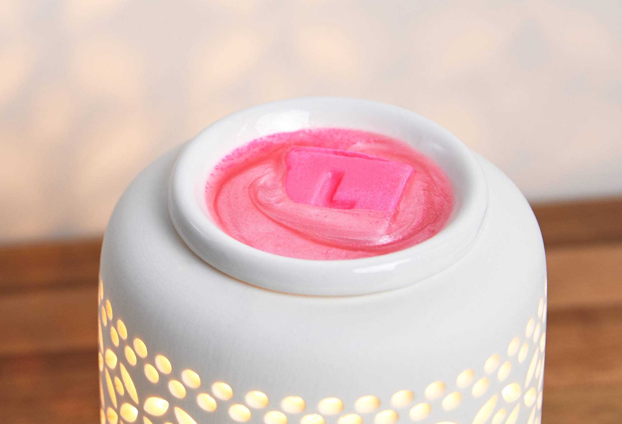 Image shows the Snow Fairy LUSH melt in a lit, white wax burner as it turns into a shimmering pink liquid.