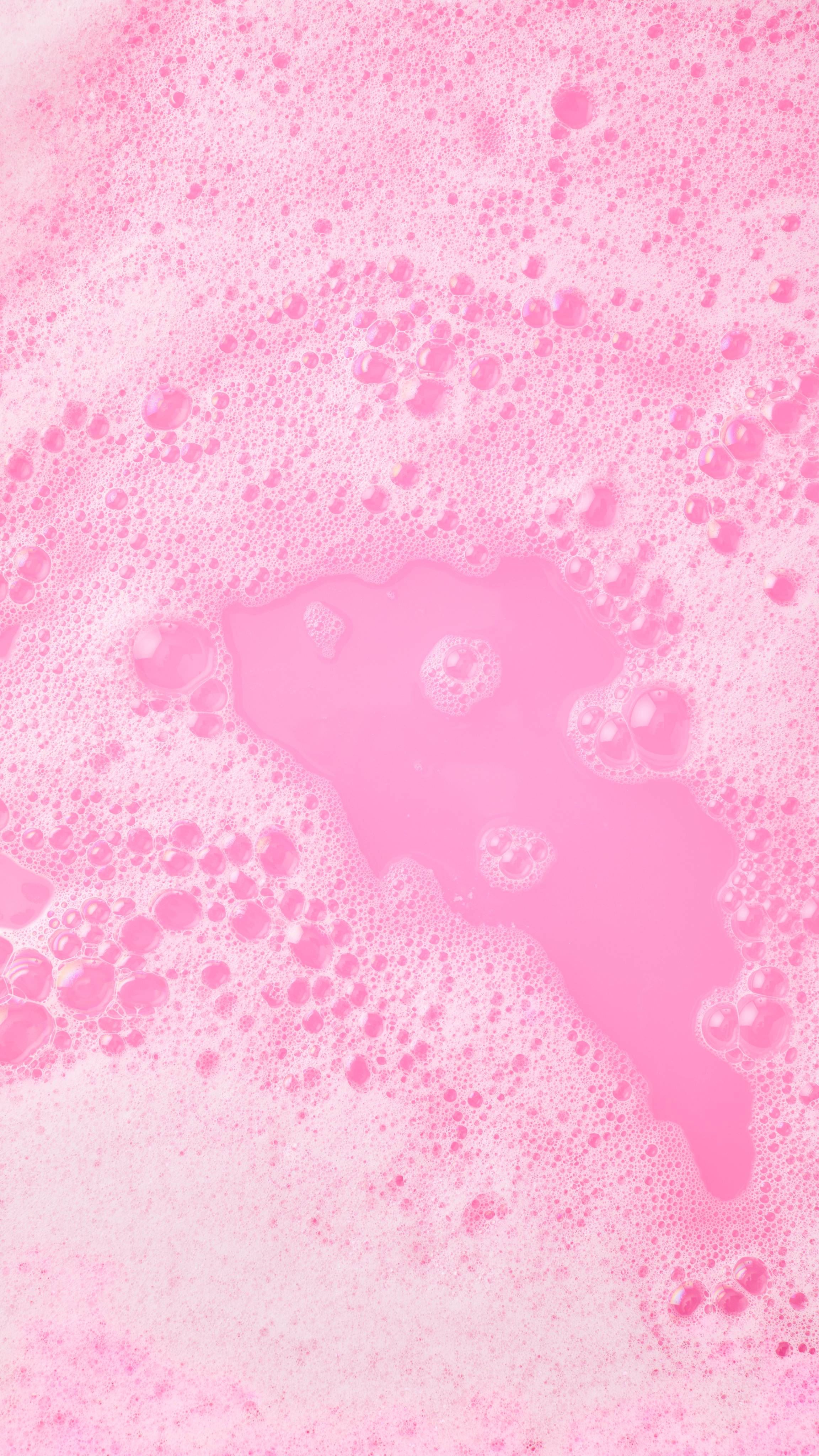 The image shows an aerial view of the bath after using the pink and white-spiralled The Big Snow Fairy Roll bubble bar. The water has been turned a bubblegum-pink colour, bordered with thick mountains of white bubbles.  