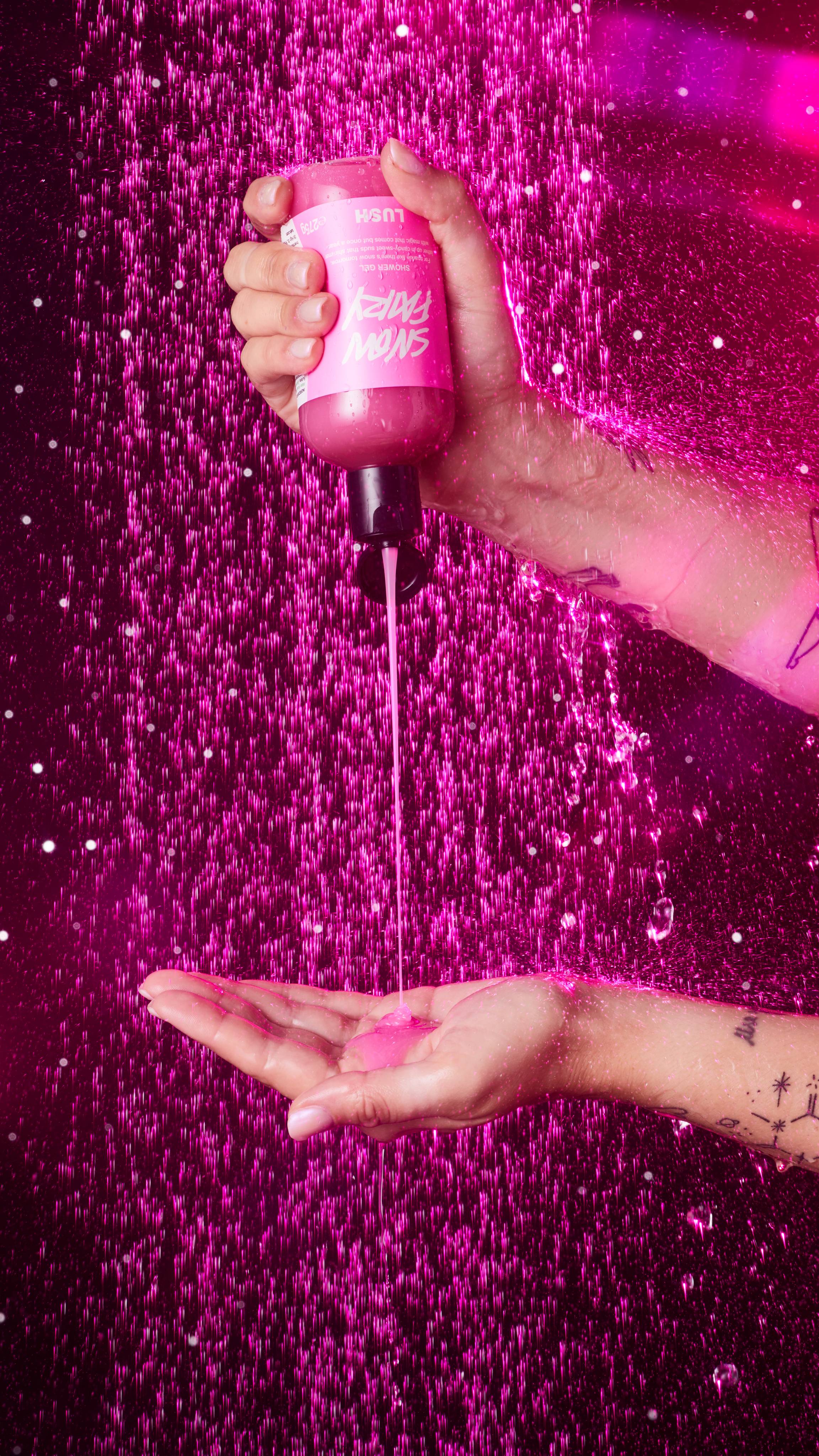 Image shows the model squeezing the bottle of Snow Fairy shower gel into their hand under running shower water. 