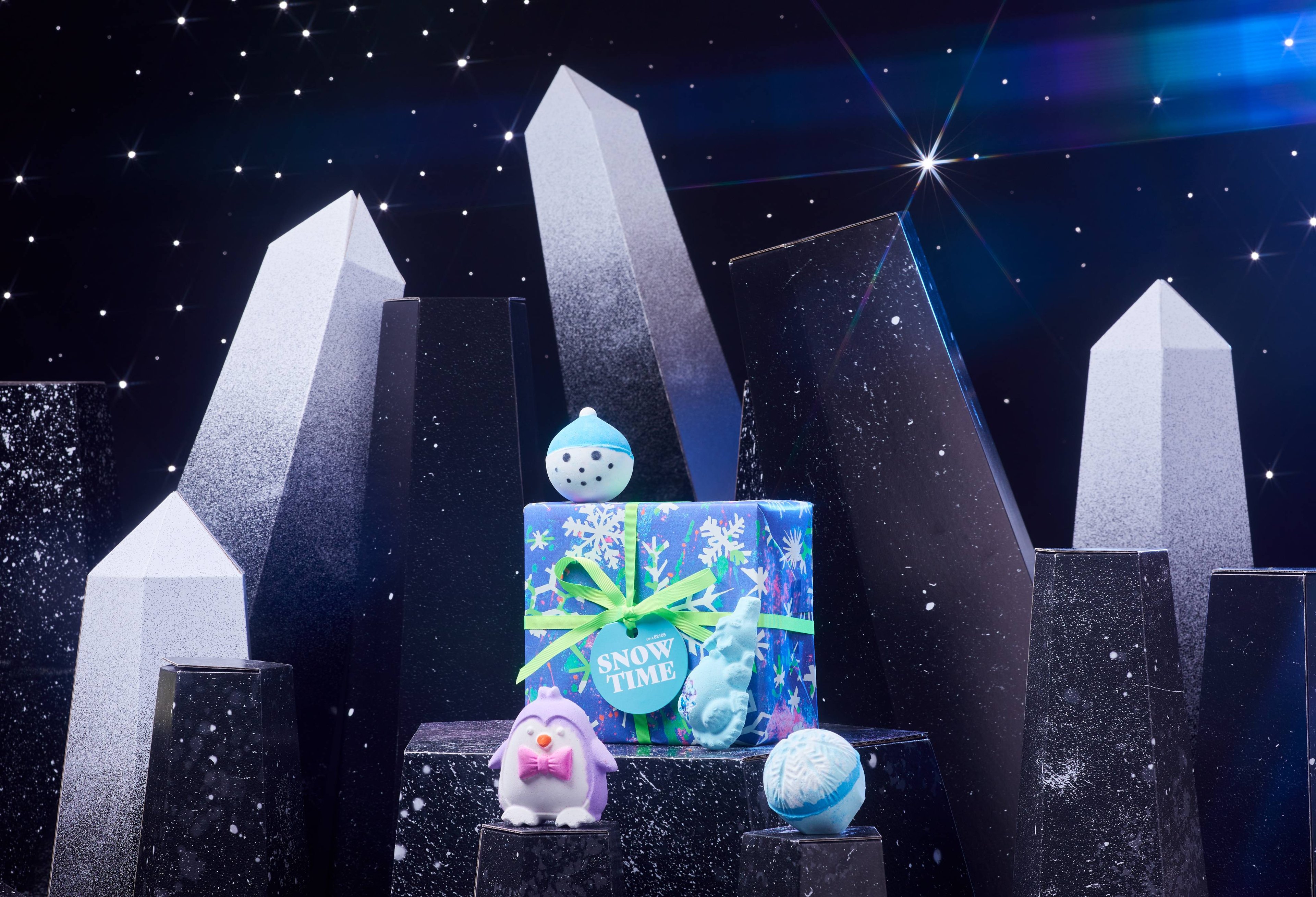 Snow Time gift box and its four included products are on a dark chromatic platform among geometric shapes. 