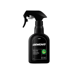
A black, curvy spray bottle of Snowcake Body Spray with a black trigger nozzle, centered on a black background. The label is black with white text detailing the product name and description, and it features a bright green "LUSH CLUB" sticker.