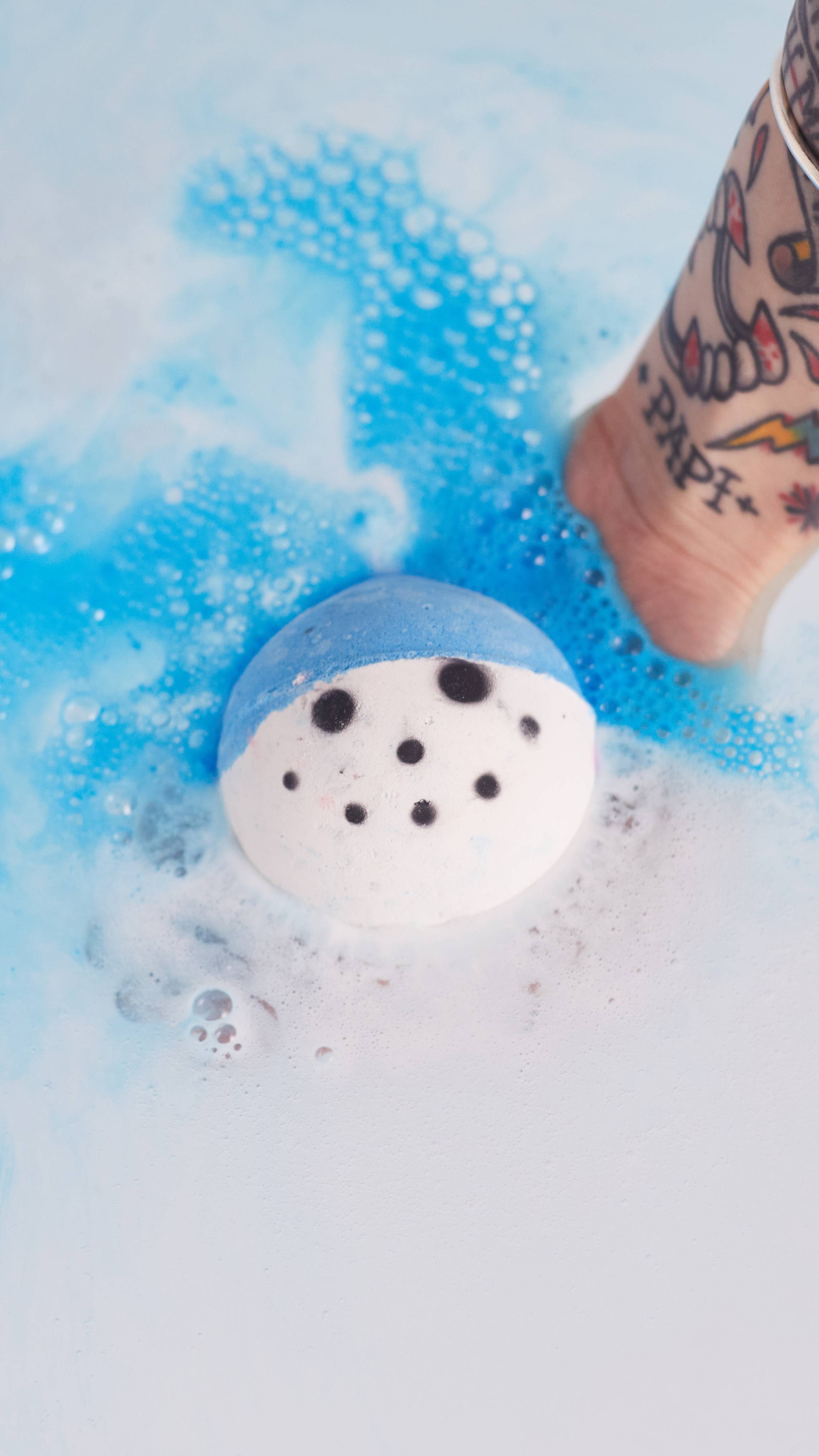 Image shows the model gently placing the Snowy bath bomb into water as the face and blue hat dissolves.