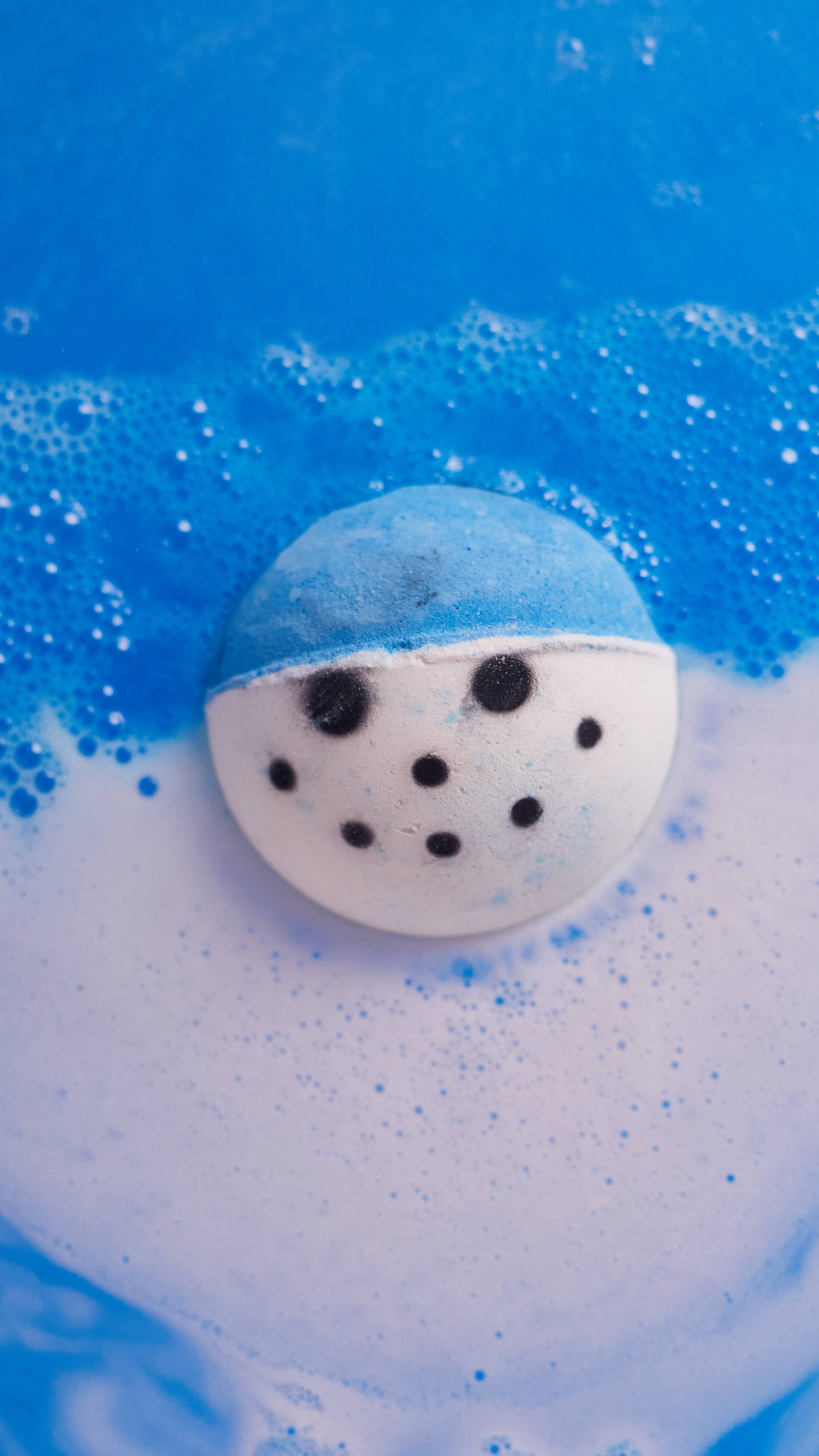 Image shows the Snowy bath bomb in the bath water surrounded by thick blue and white creamy foam.