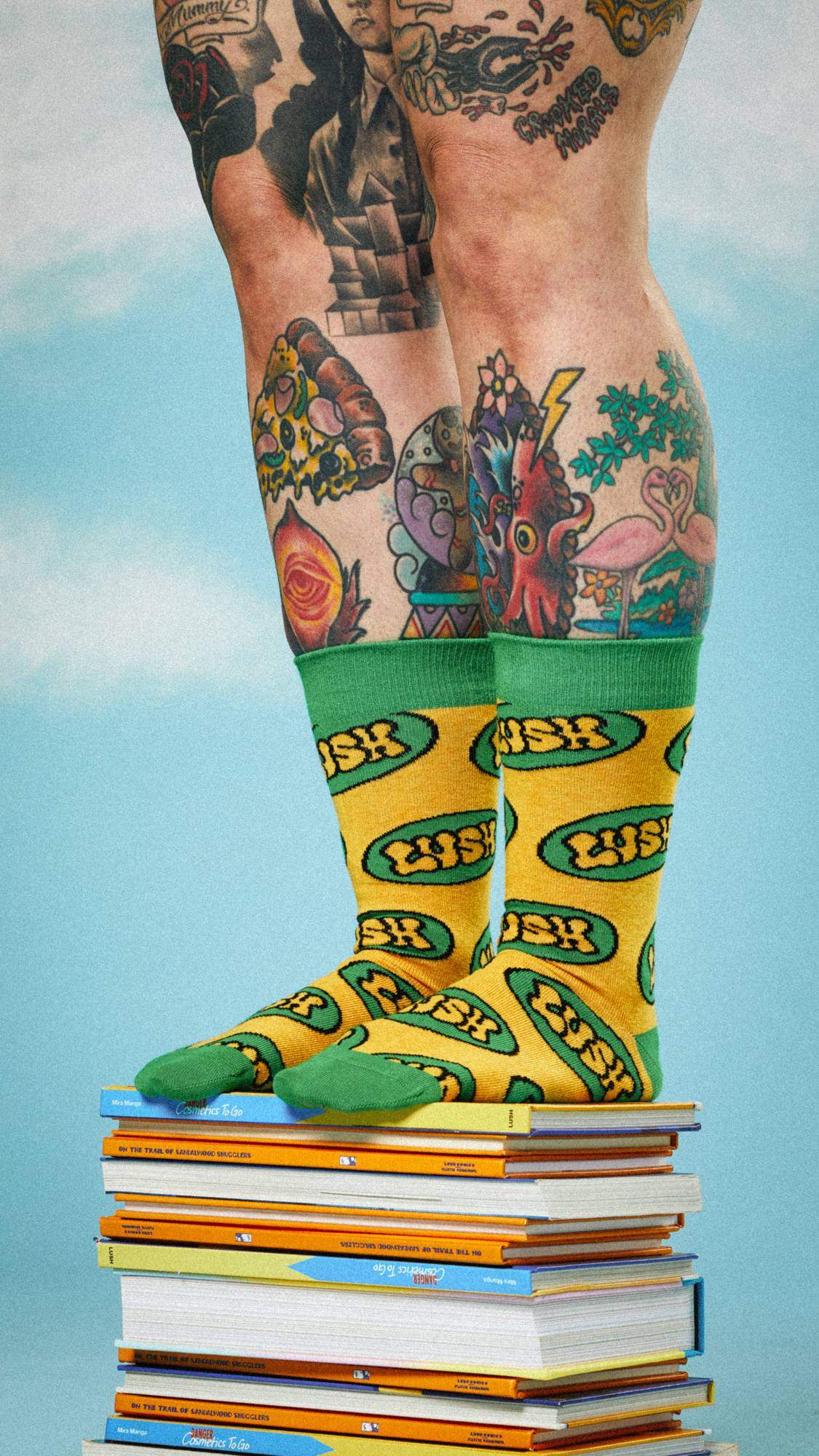 Model is heavily tattooed as we see them wearing the Retro Bubble Lush socks pulled to their calves, stood on a stack of books