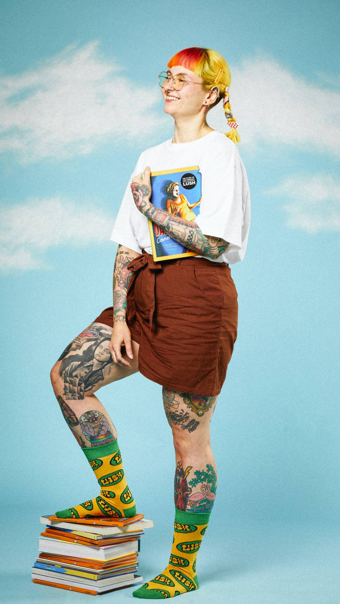 Model is on a sky-style backing in a simple outfit wearing the Retro Bubble Lush socks with one foot on a stack of books.