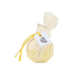 Soothing Chamomile And Yarrow Cataplasm. A yellow, spherical bath bomb wrapped in muslin fabric, tied with a knot and yellow string and product tag which reads "Don't unwrap, dunk this in your bath"