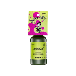 A bottle filled with dark green Lush shower gel, topped with a bright pink and green cardboard tag illustrated with a magician character and the text "Sorcery"