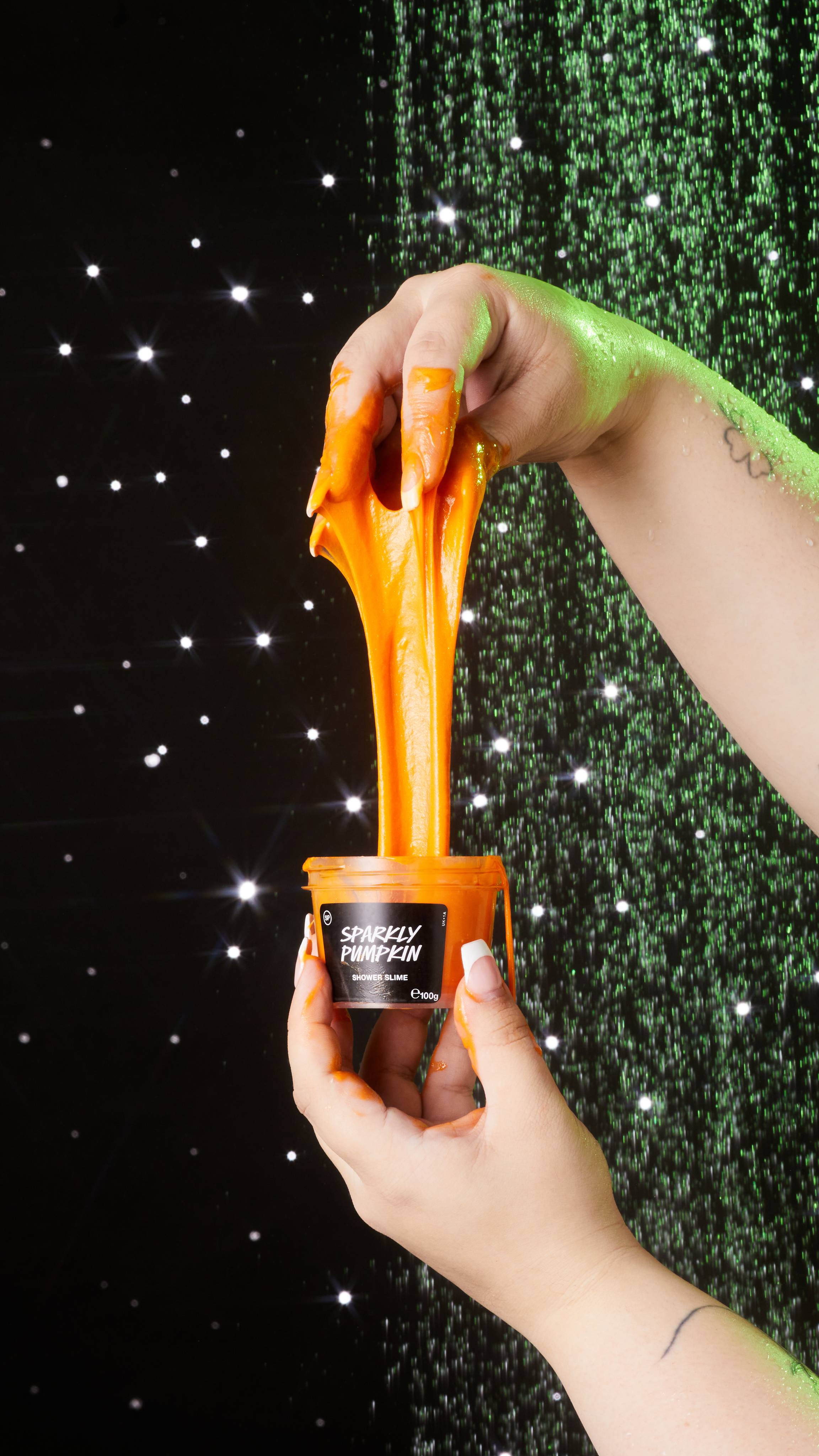 Close-up of model holding the product pot with one hand as they stretch out the neon-orange, viscous slower slime.
