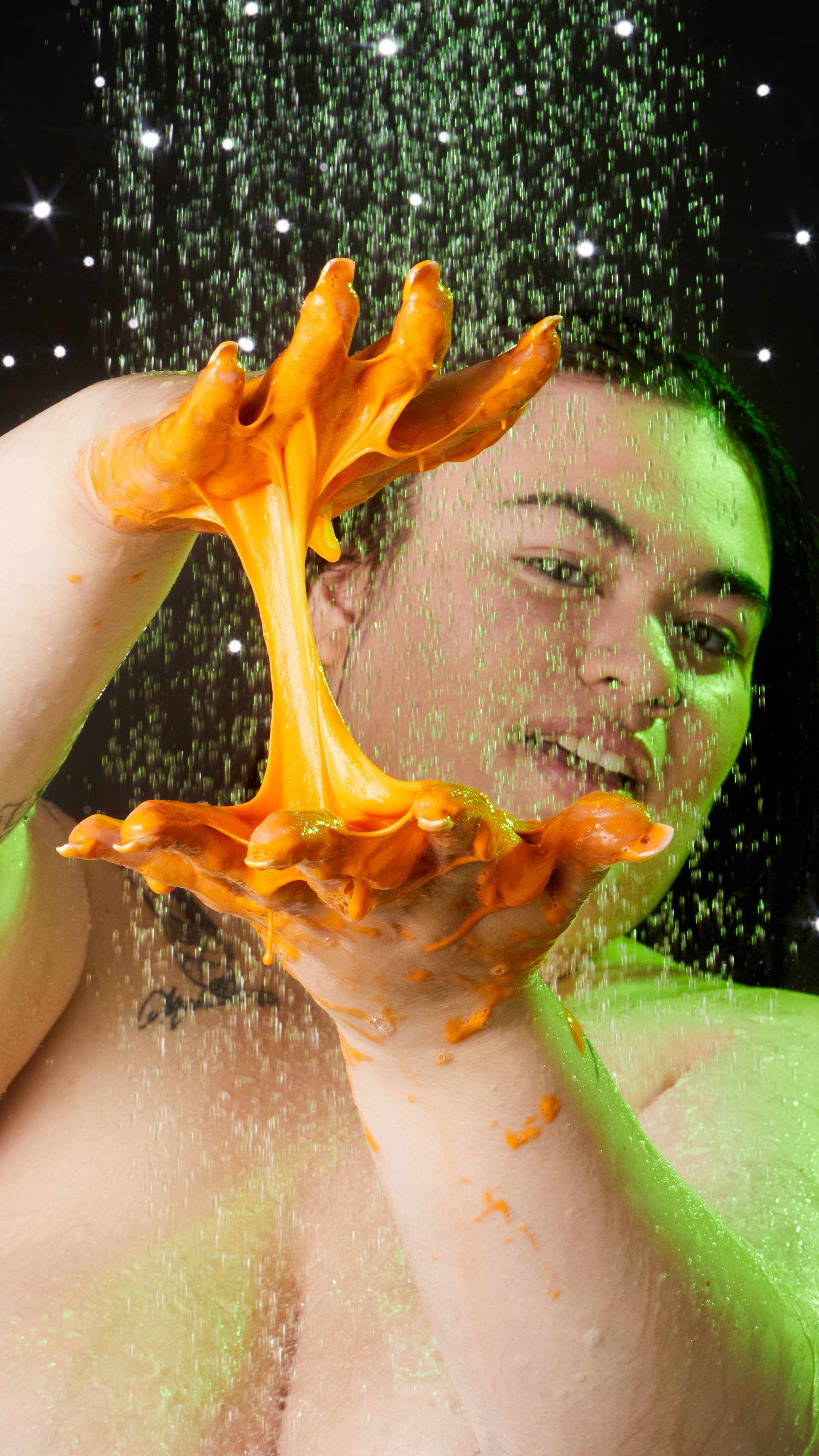 A close-up image of the model's hands as they are in the shower. They are separating and stretching the gooey slime apart.