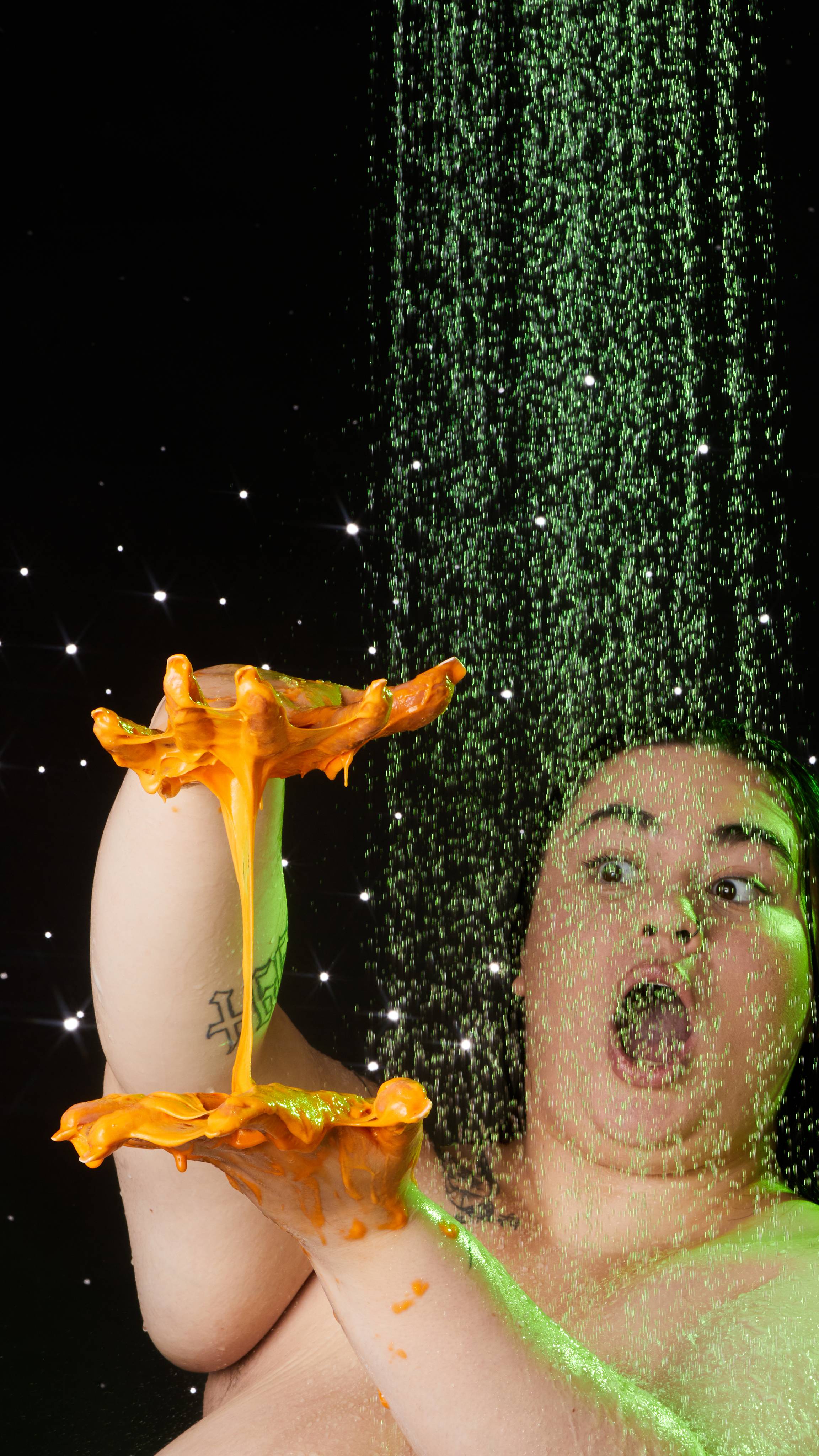 Model stands under the shower with both hands in front of them stretching the product creating a fun, orange, slimy webbing.
