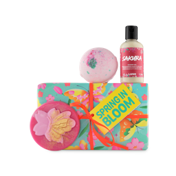Spring in Bloom. A rectangular gift box wrapped in light, floral paper and tied with an orange ribbon and gift tag. Three themed products sit around the box including a shower gel, bath bomb and soap.