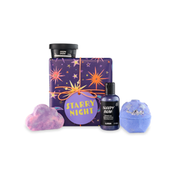 Starry Night. A, off-square gift box wrapped in dark purple paper with colourful star designs, tied with orange twine and a purple gift tag. Four Lush products sit on and around the gift box.
