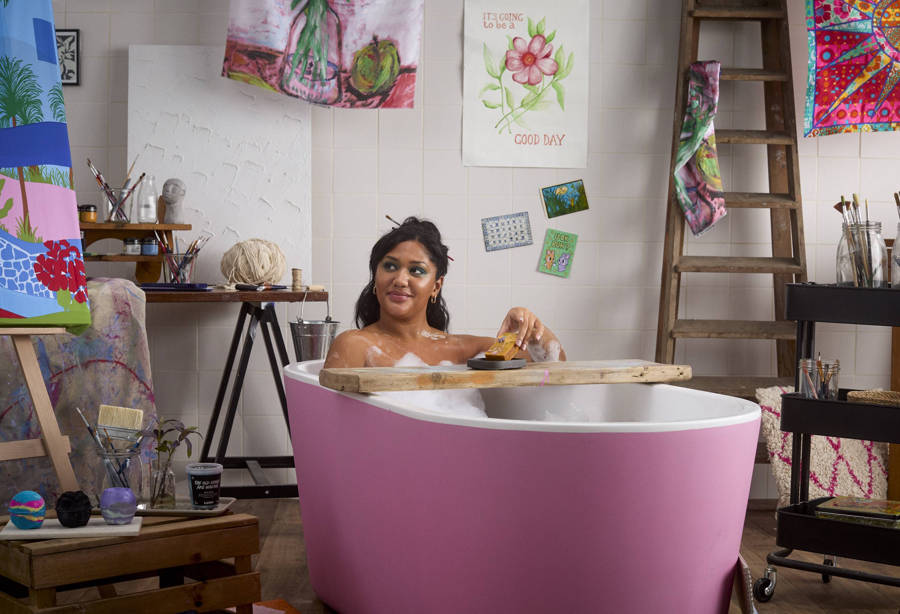 The image shows the model in a pink bathtub in the middle of an art studio. 