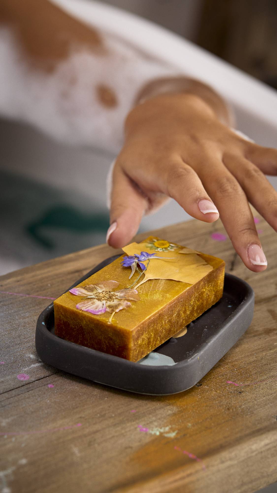 A close-up image of the model's hand reaching for the Sticky Syrup soap in the Kaleidoscope soap dish. 