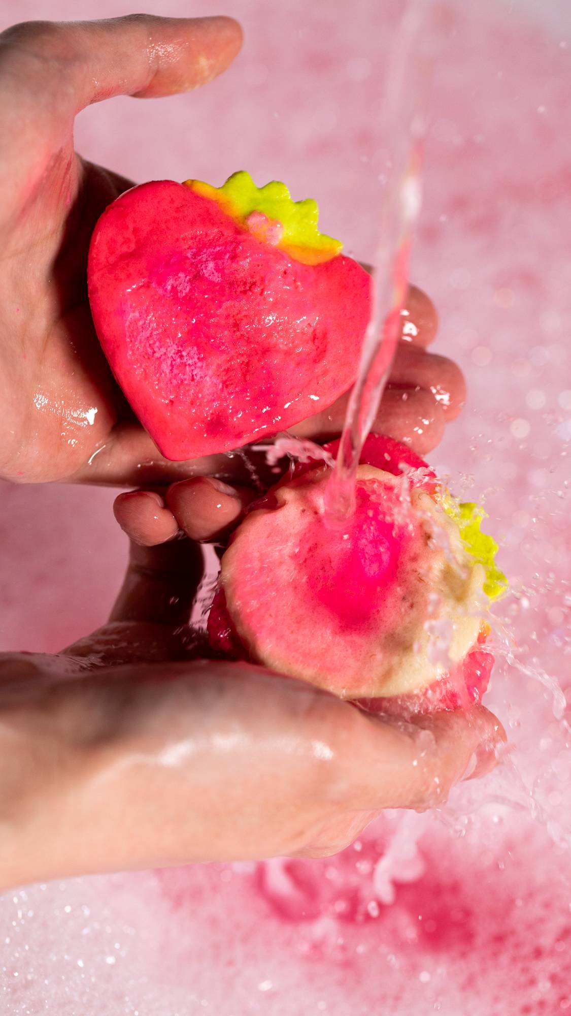 The image shows a close-up of the model who has broken the bubble bar in half and is holding both halves under running water.