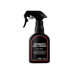 A recycled black plastic LUSH body spray bottle with a trigger nozzle stands upright with a red rimmed label with white text that reads "Strawberry Feels Forever Body Spray".