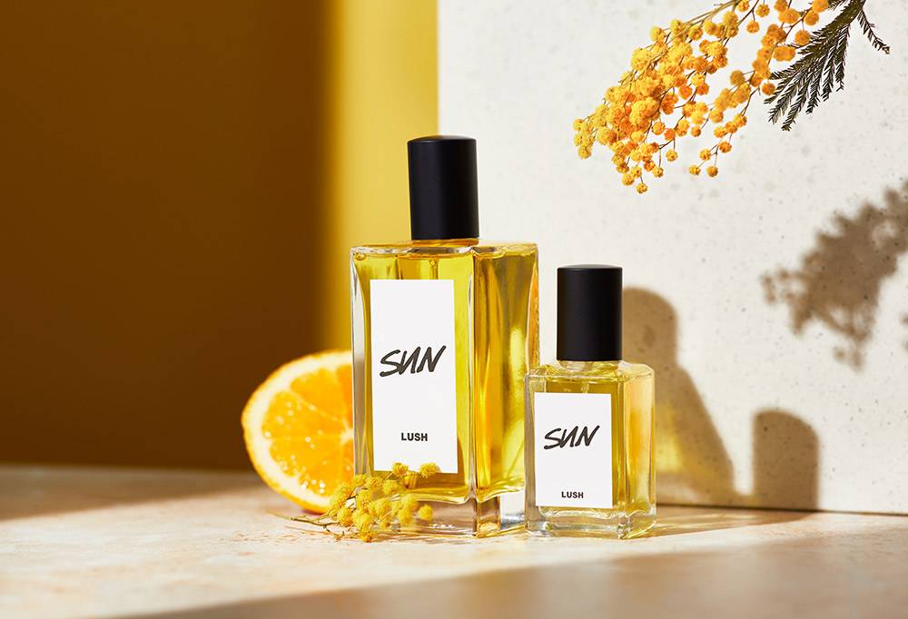 Sun perfume is displayed alongside a slice of fresh lemon and yellow mimosa flowers on a yellow and white background.